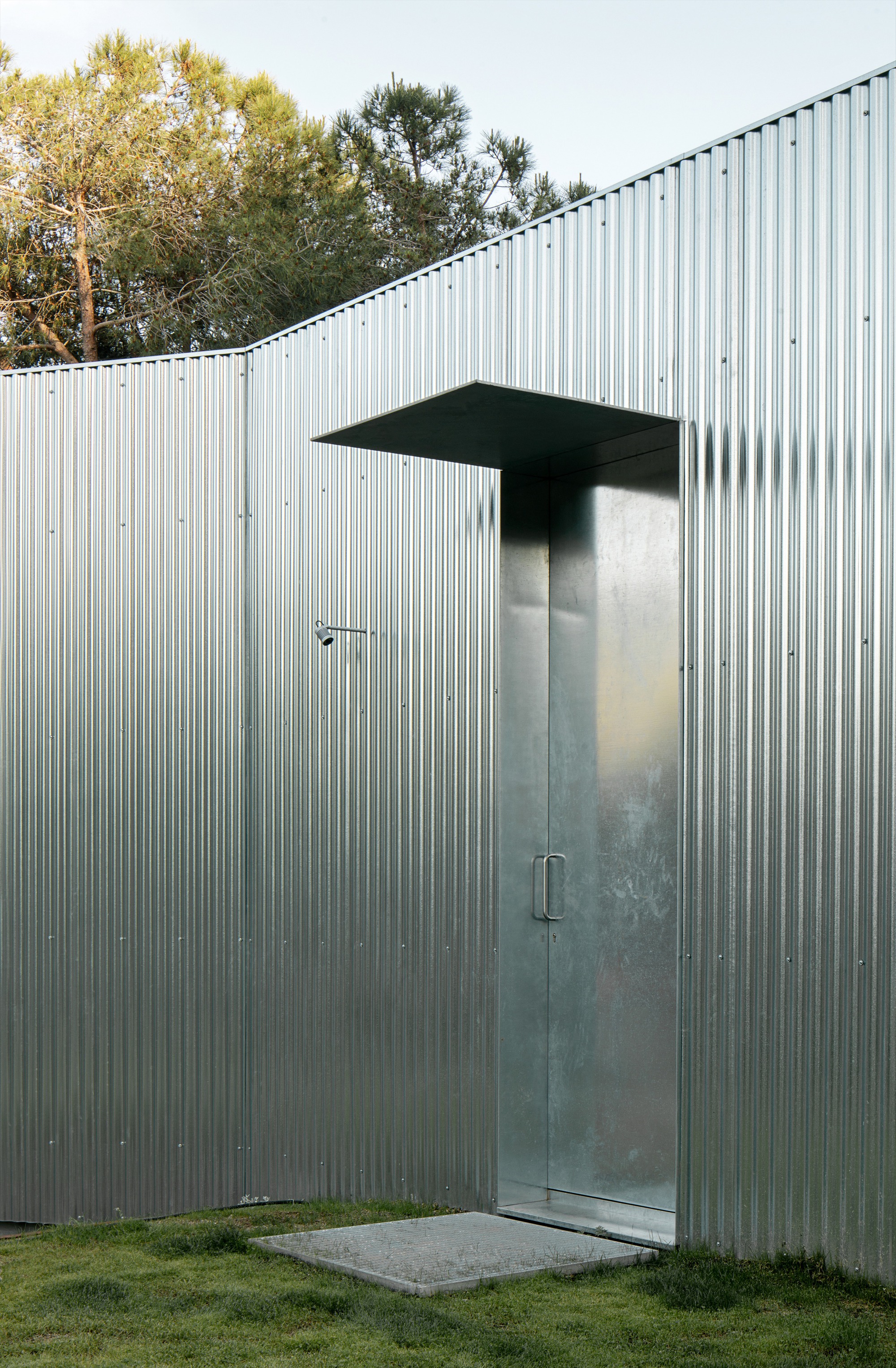 Exterior entrance with glass door and canopy set into corrugated metal facade with trees behind