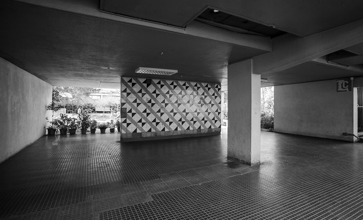 Covered parking area with geometric concrete screen wall and small planted pots near columns