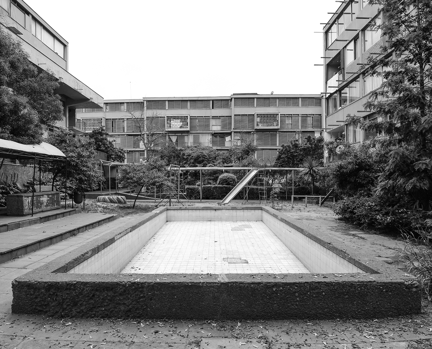 Drained swimming pool in a courtyard garden surrounded by three-story residential blocks and trees