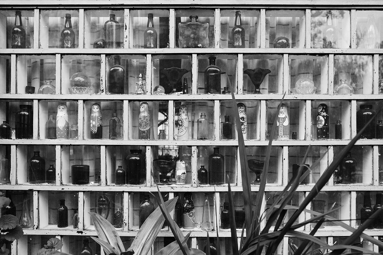 Shelving unit with white painted timber grid holding glass bottles and objects behind diagonal bracing