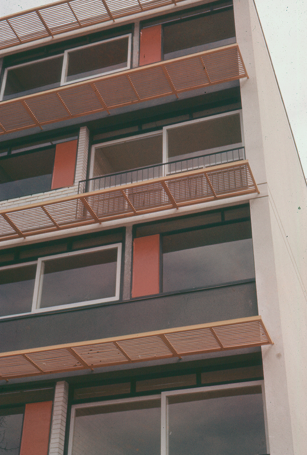 Stacked balconies with horizontal timber slat screens, orange panels and exposed ventilation ducts