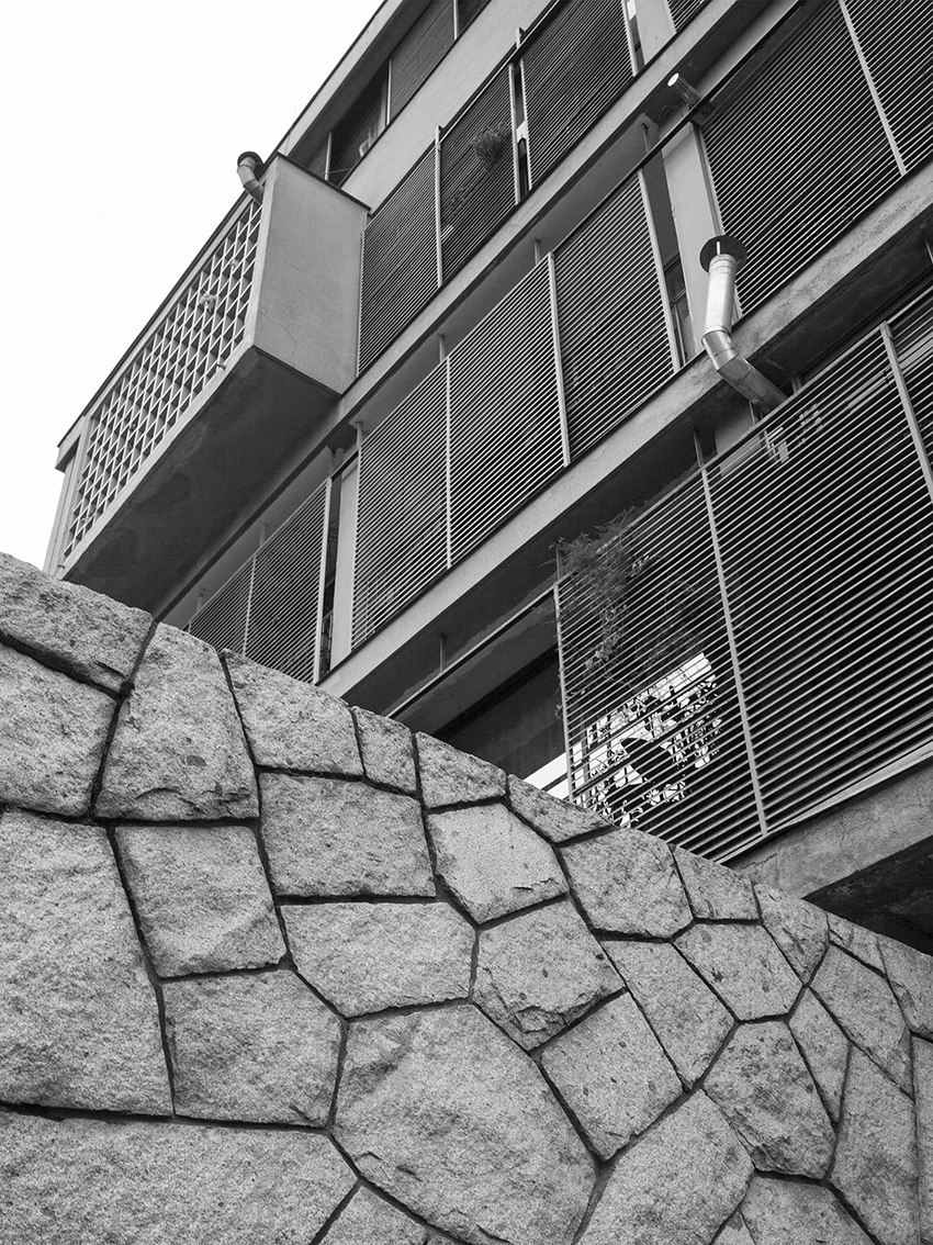 Facade with horizontal louvered screens above a rough-cut stone retaining wall at the base