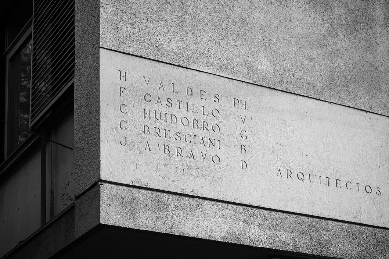 Close-up of incised lettering on a textured concrete corner panel listing architect names