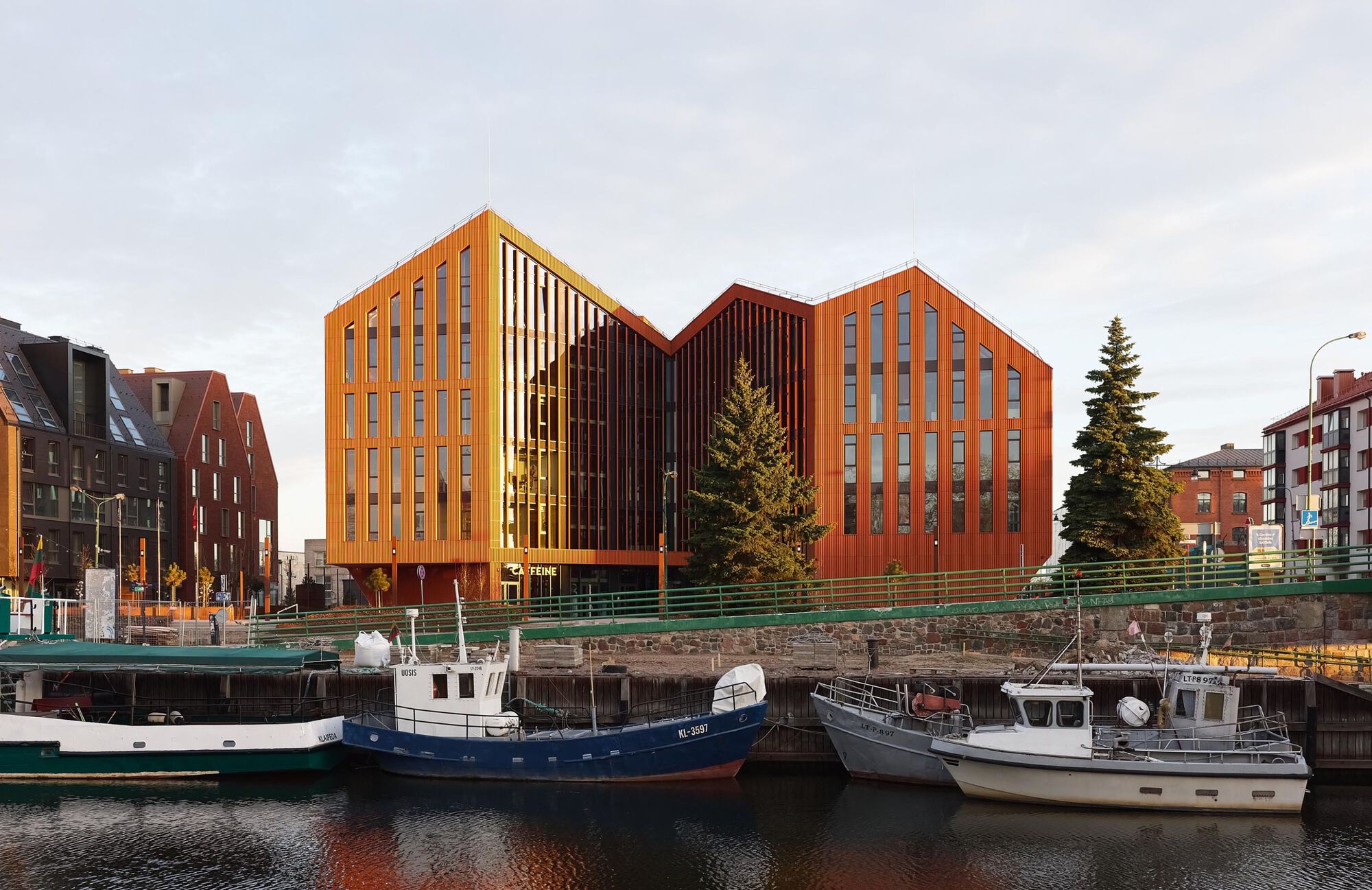 Harborside view of the three connected volumes at dusk with boats docked along the quay