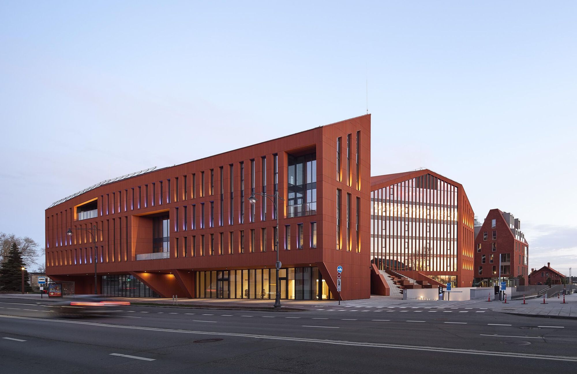 Street view of the perforated terracotta facade at twilight with ground floor glazing illuminated