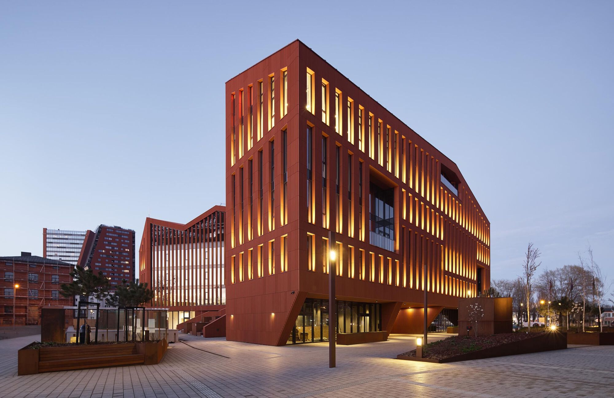 Corner view at dusk showing interior lighting through the vertical terracotta louvers and courtyard planters