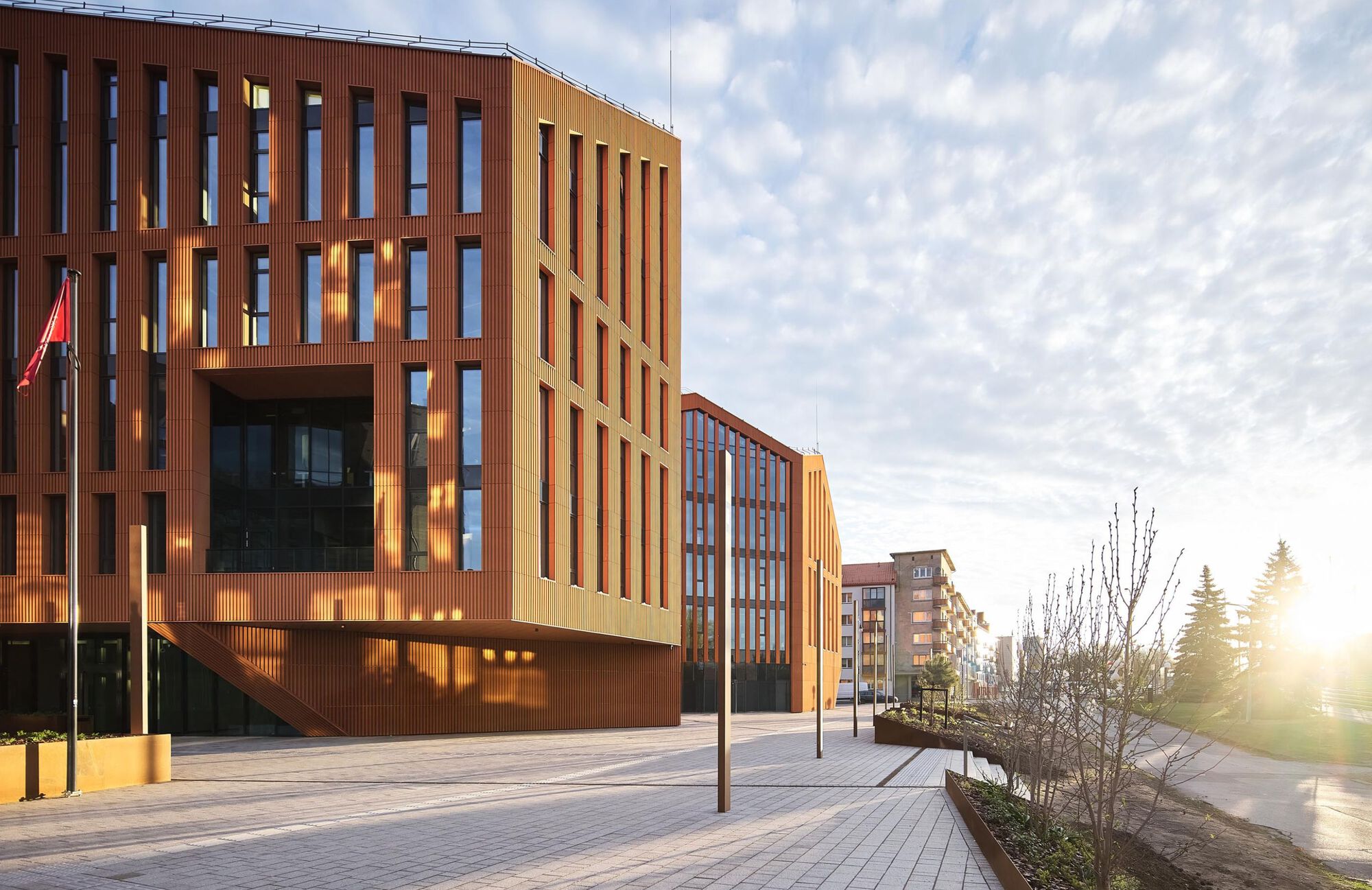 Plaza facing the terracotta-clad facade with deep vertical openings and planted beds at dawn