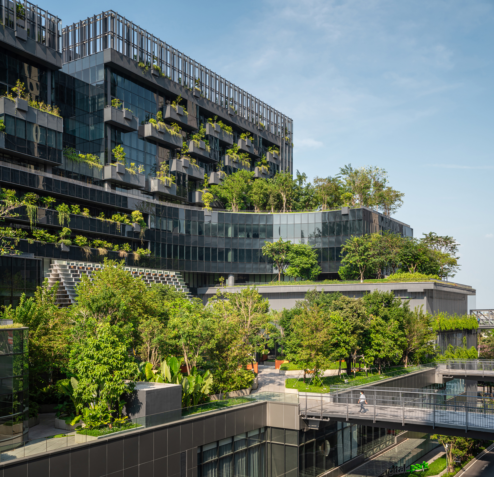 Multilevel planted terraces with trees emerging between glass facades and green roof gardens
