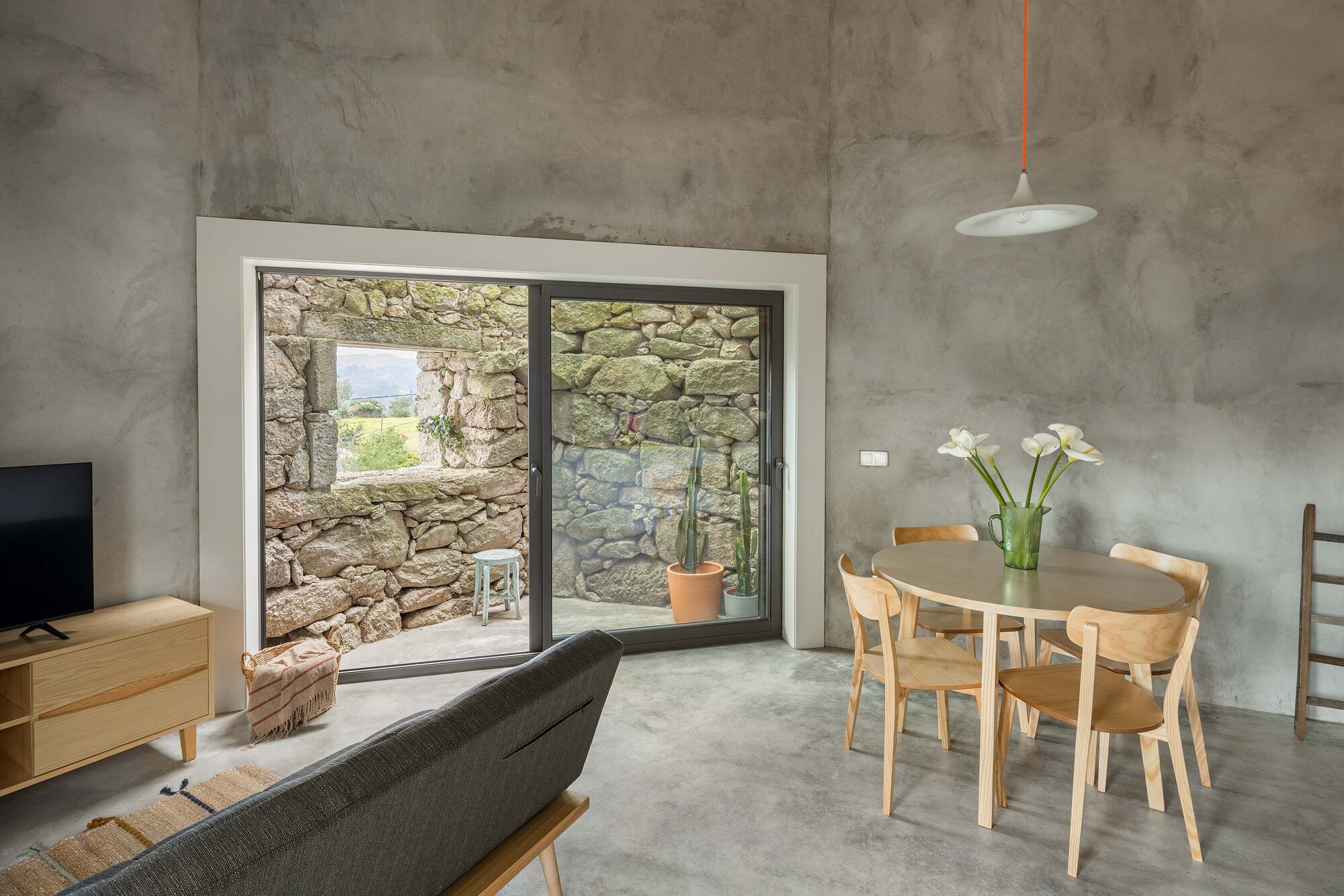 Polished concrete floor and dining table framed by glazed opening revealing the stone wall courtyard beyond