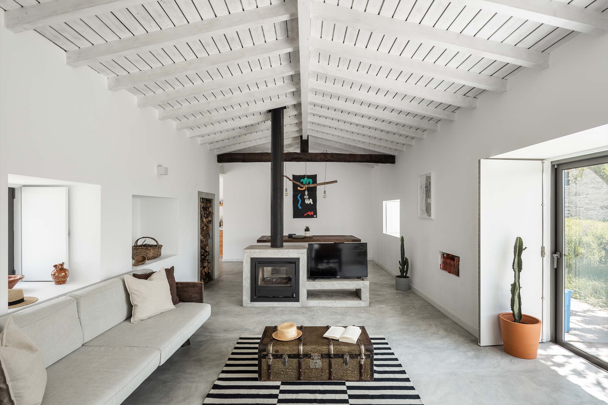 Living room with white painted timber ceiling, exposed dark beams and a concrete masonry fireplace