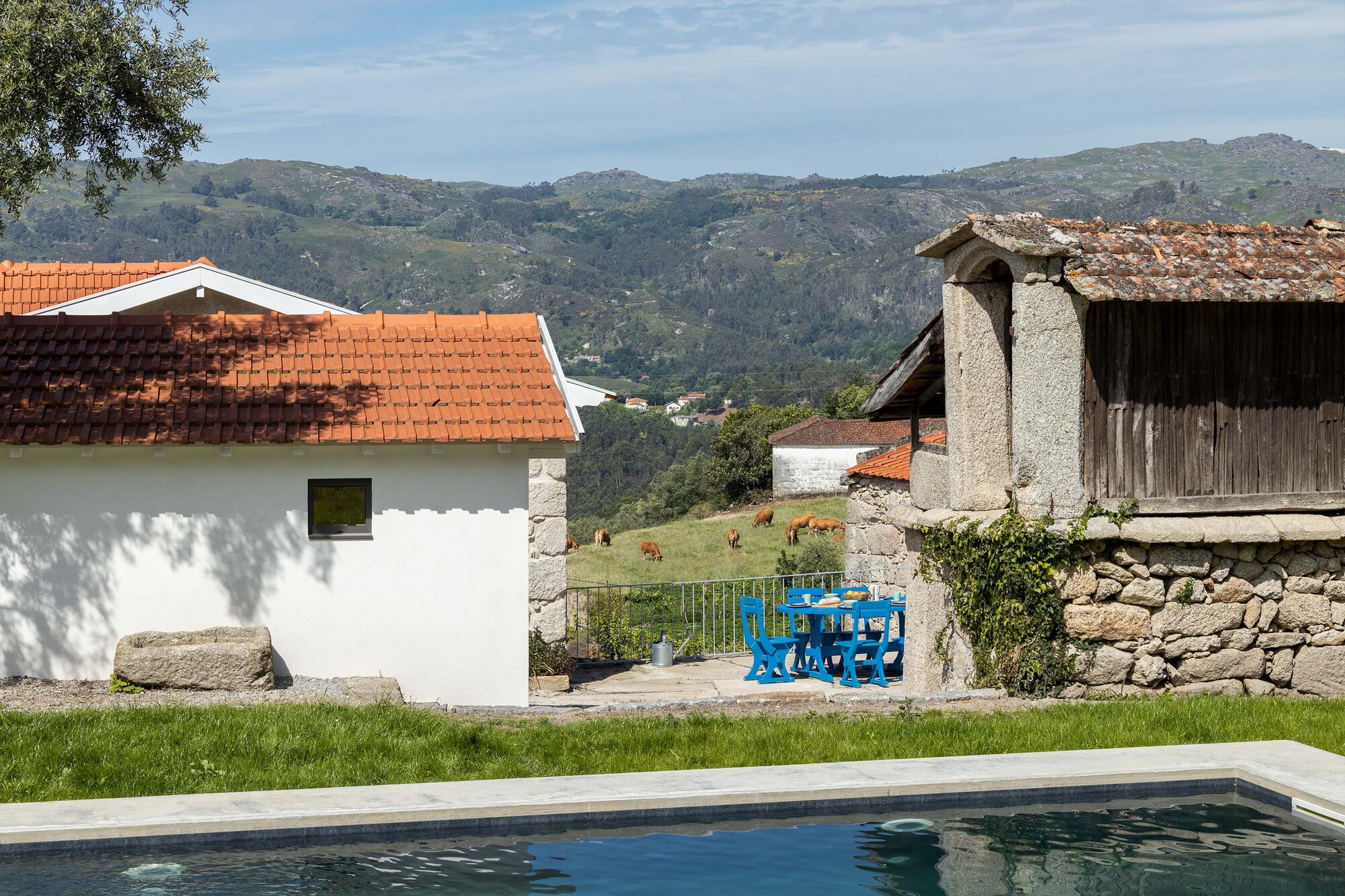 Swimming pool edge with white plastered volume and blue painted furniture against mountain backdrop