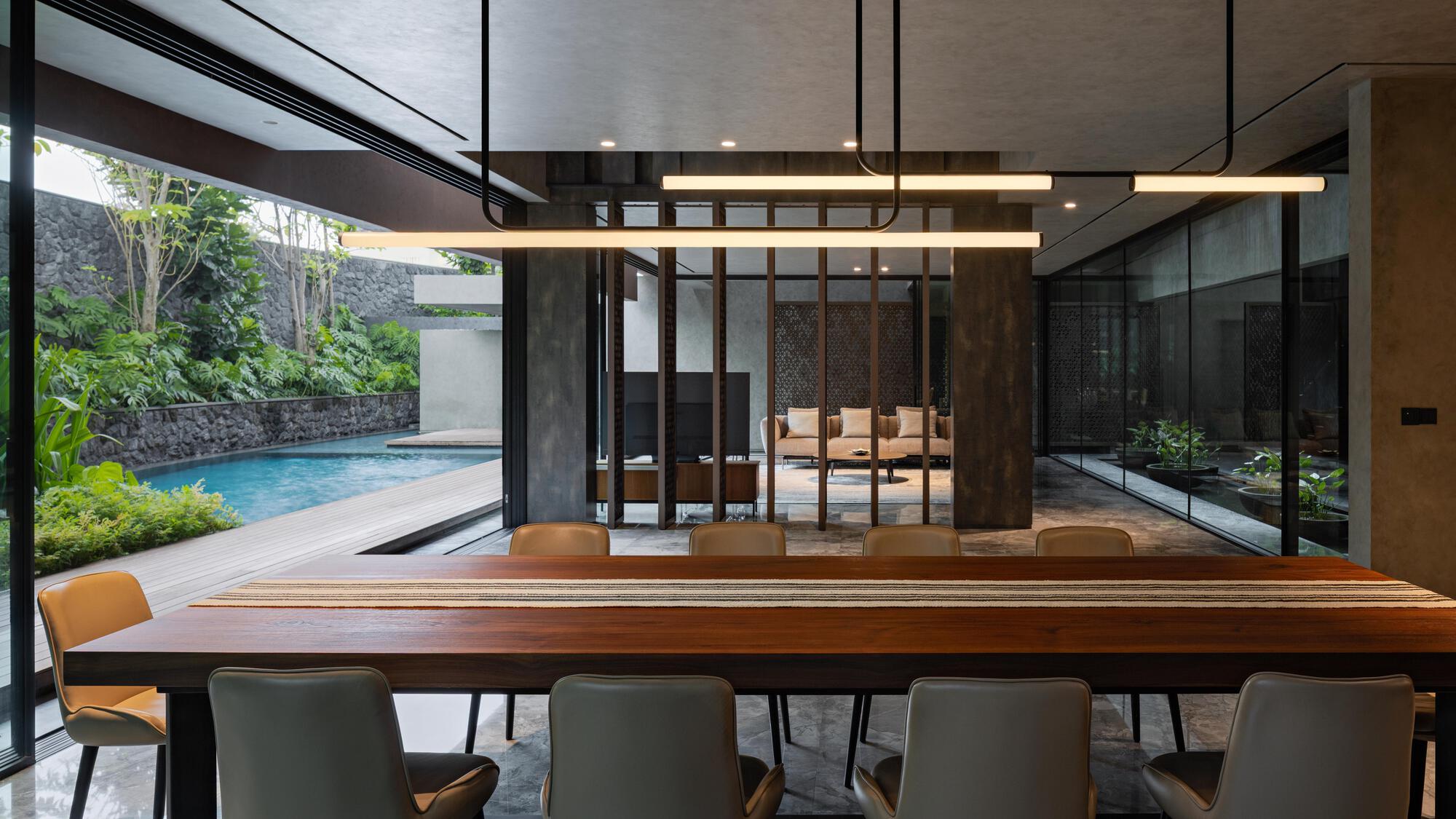 Dining area with linear pendant lights opening to pool terrace through floor-to-ceiling glass
