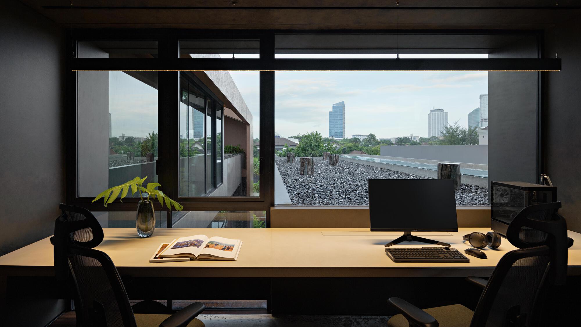 Office workspace with full-height glazing overlooking a gravel roof terrace and distant skyline