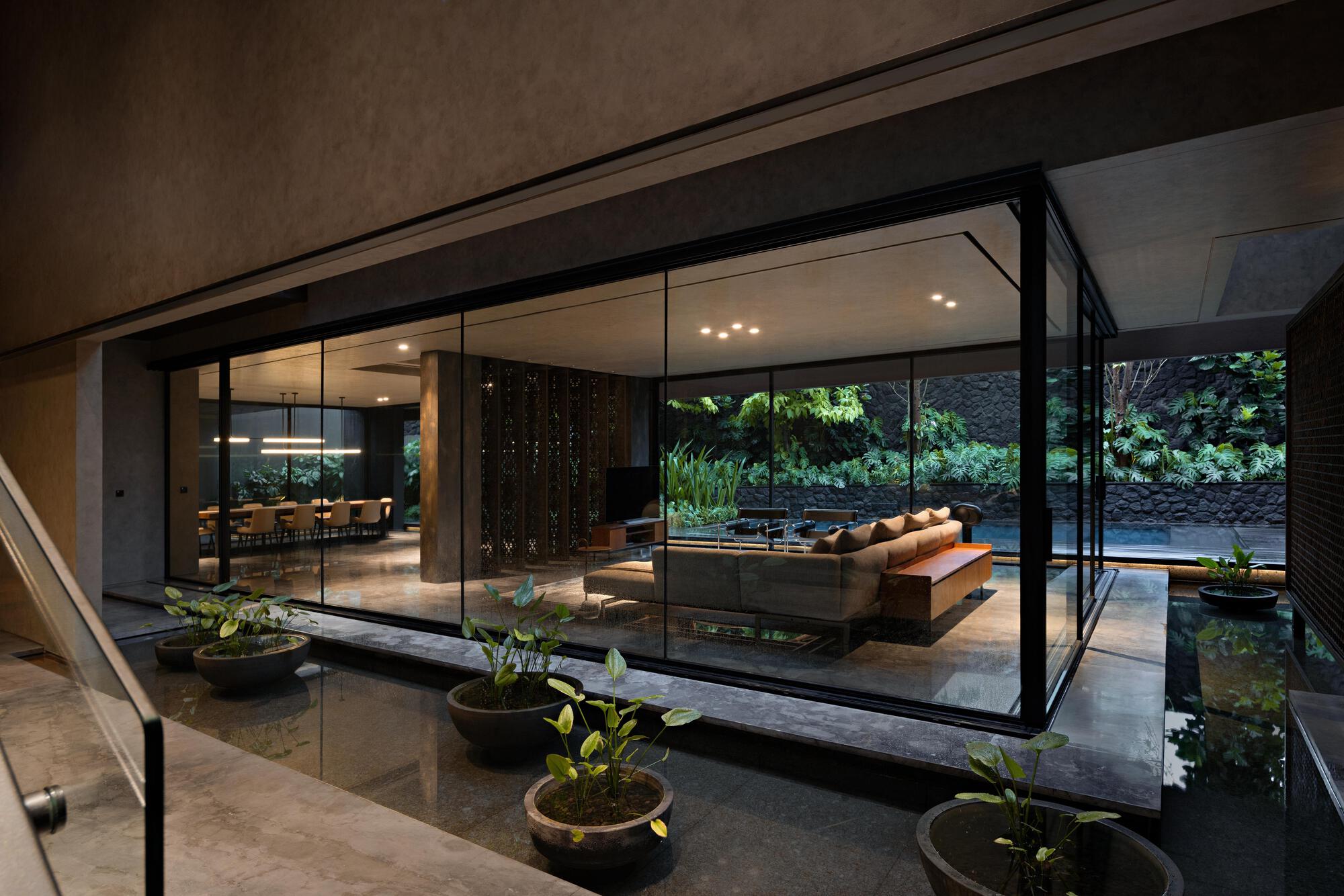 Glass-enclosed living pavilion opening onto a courtyard with planted beds and reflecting pool