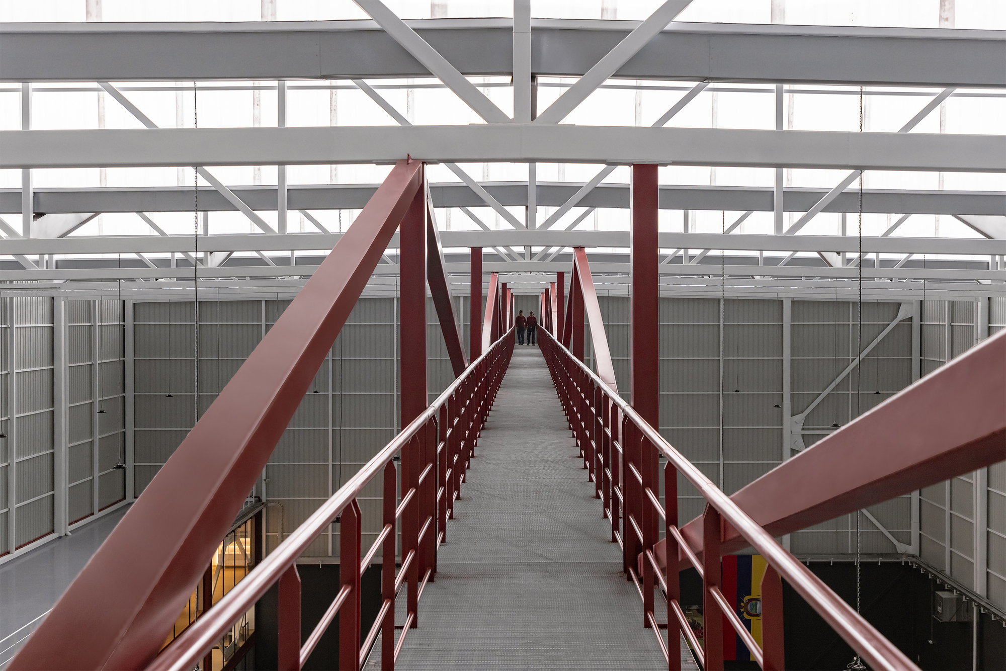 Enclosed steel bridge corridor with red railings and diagonal bracing viewed along its length