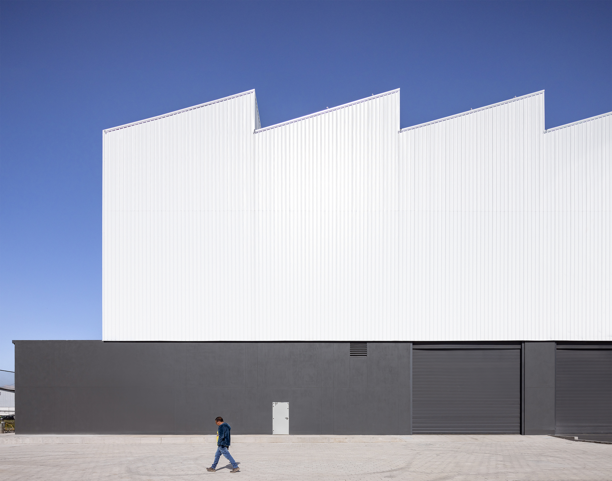Street facade with dark grey base and white sawtooth roof form against a clear blue sky