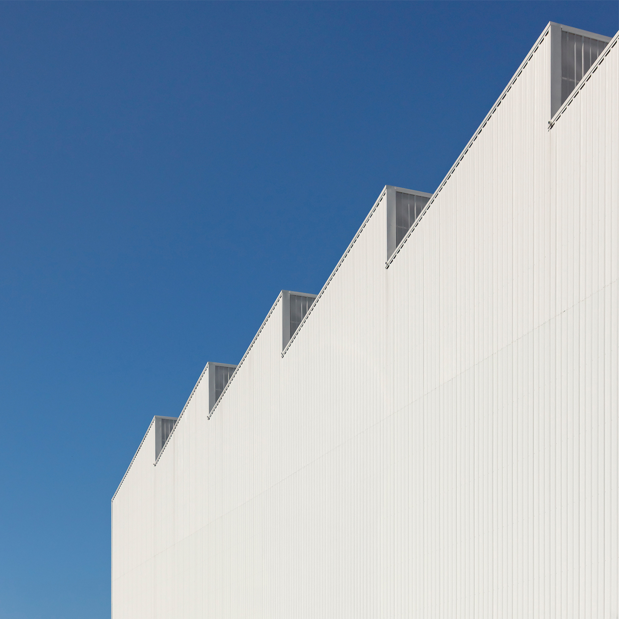 Detail of the stepped white metal roof edge with translucent panels against a clear blue sky