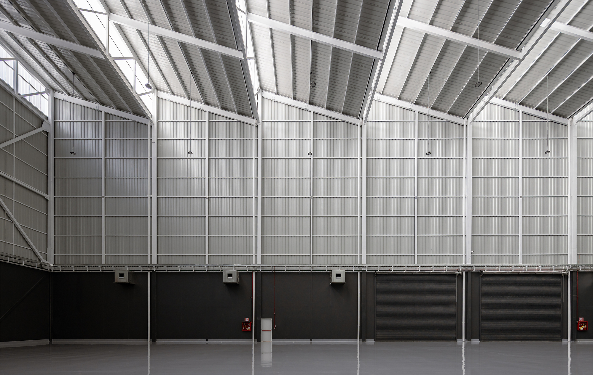 Interior wall of corrugated metal panels rising to meet angled skylights in the sawtooth roof above