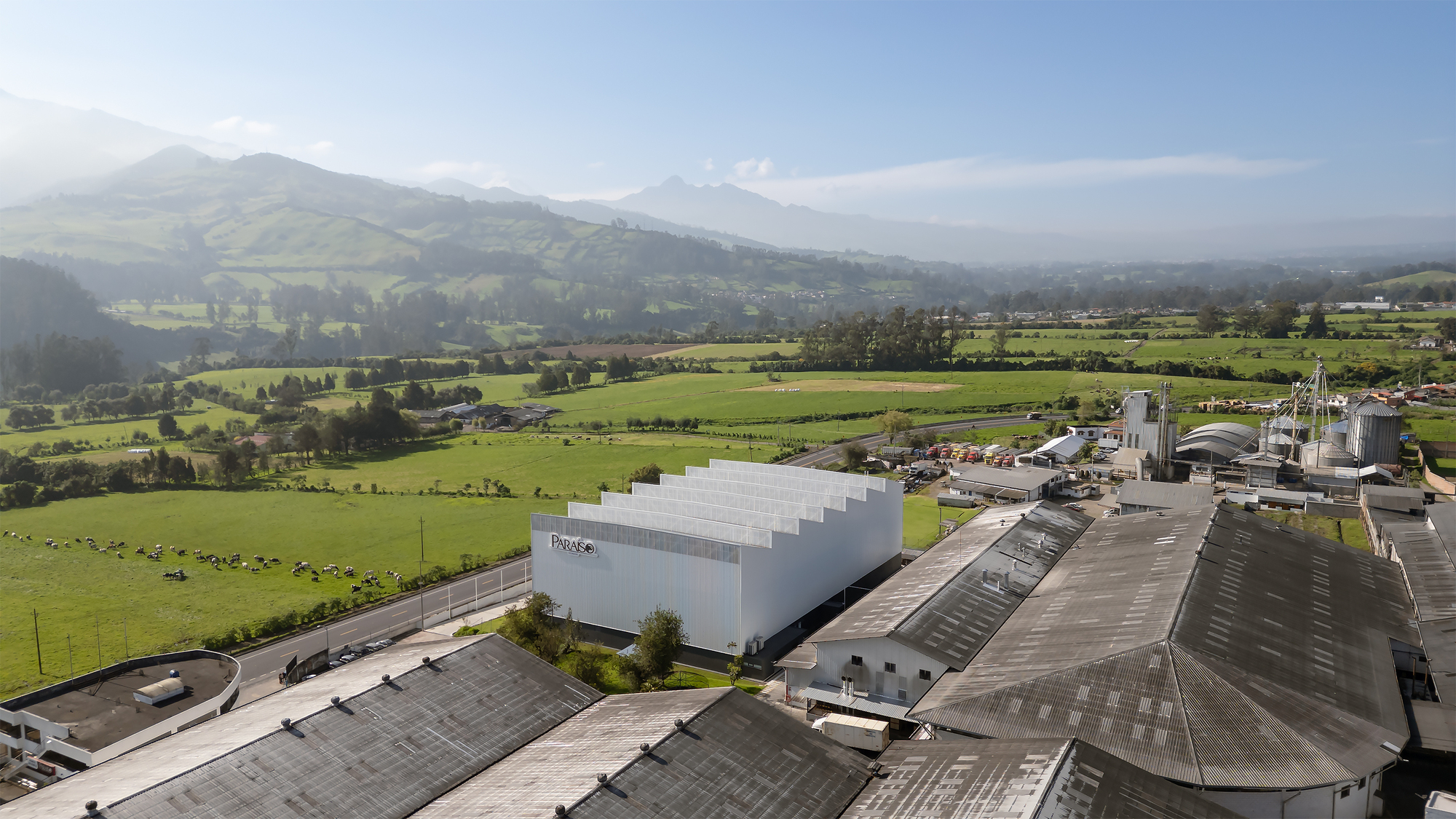 Aerial view of the sawtooth roofline and white corrugated facade set among industrial buildings and farmland