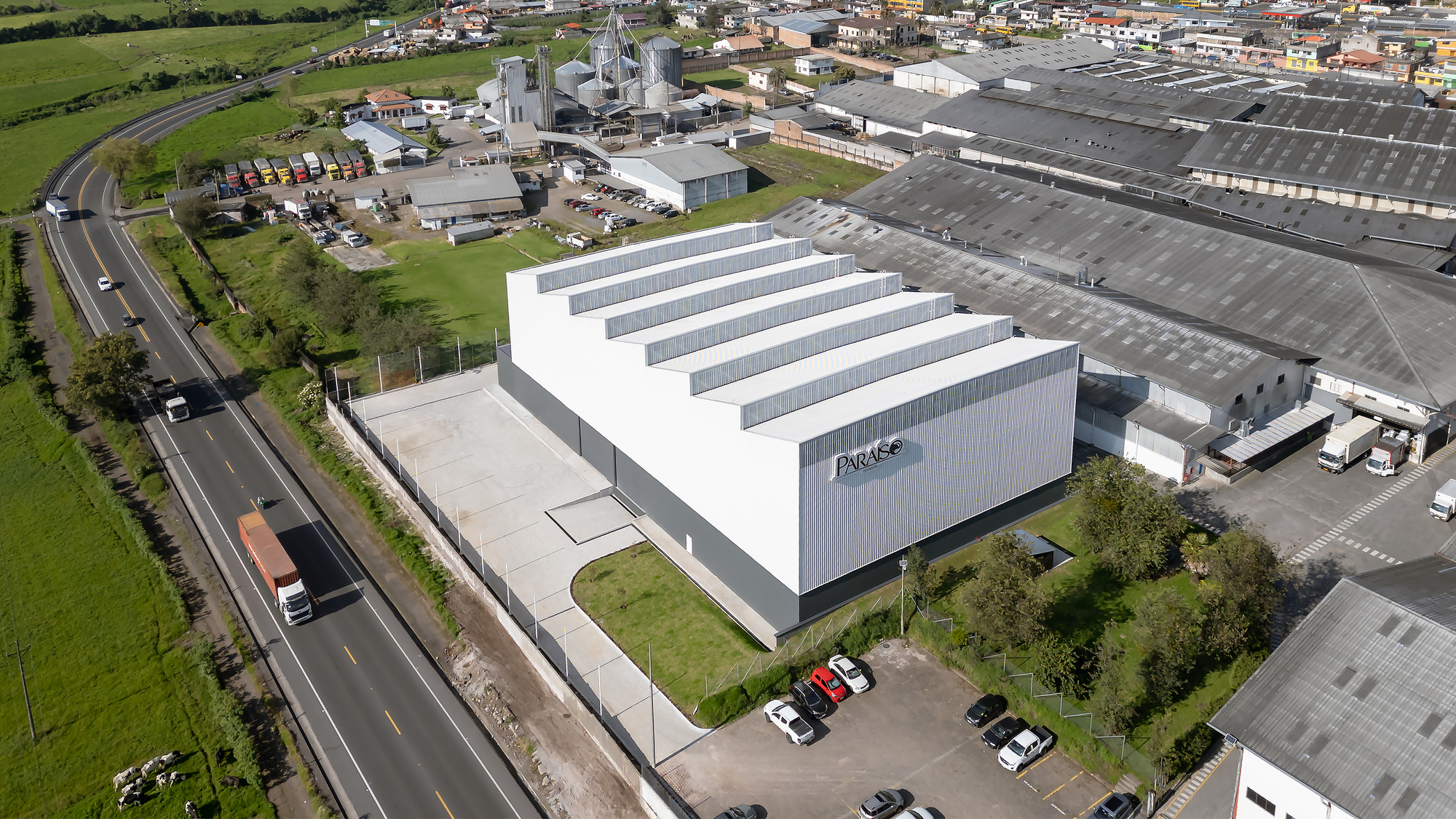 Oblique aerial view showing the stepped horizontal glazing bands across the white metal-clad volume beside a roadway