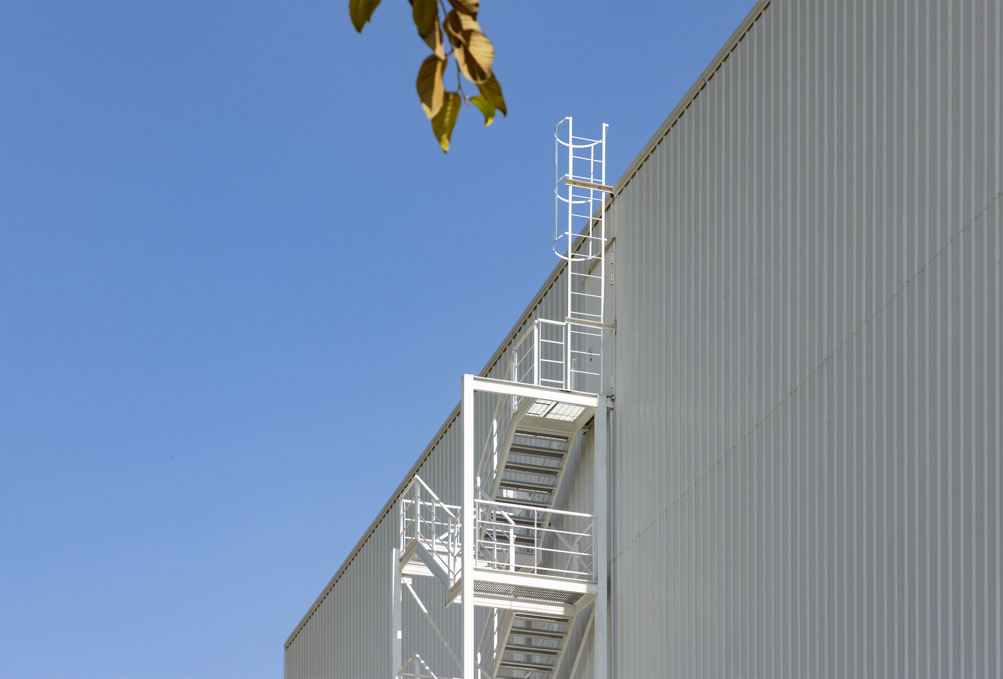 White painted steel egress stair against the corrugated metal cladding under clear blue sky