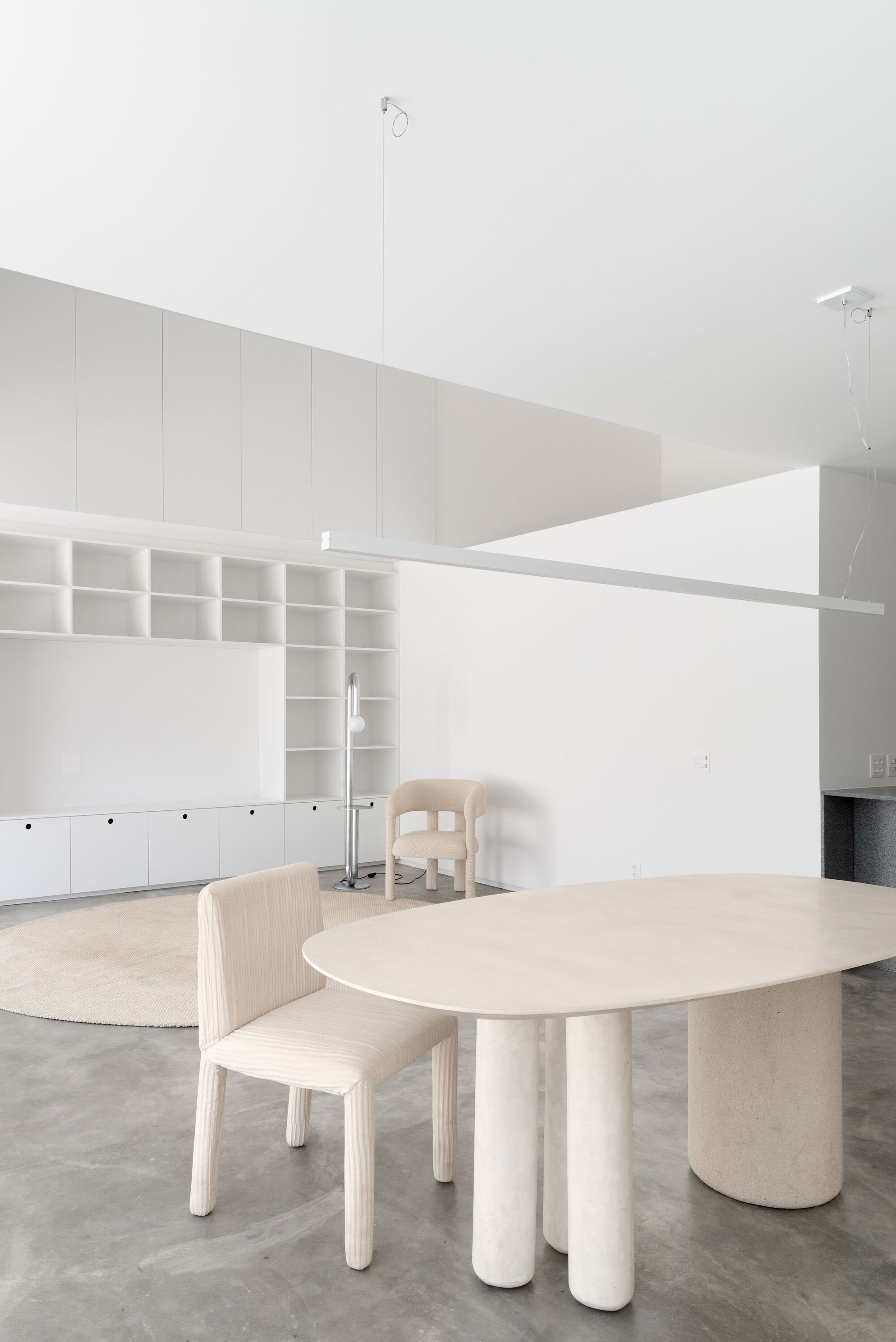 Light wood dining table with cylindrical concrete legs surrounded by wooden chairs under vaulted white ceilings