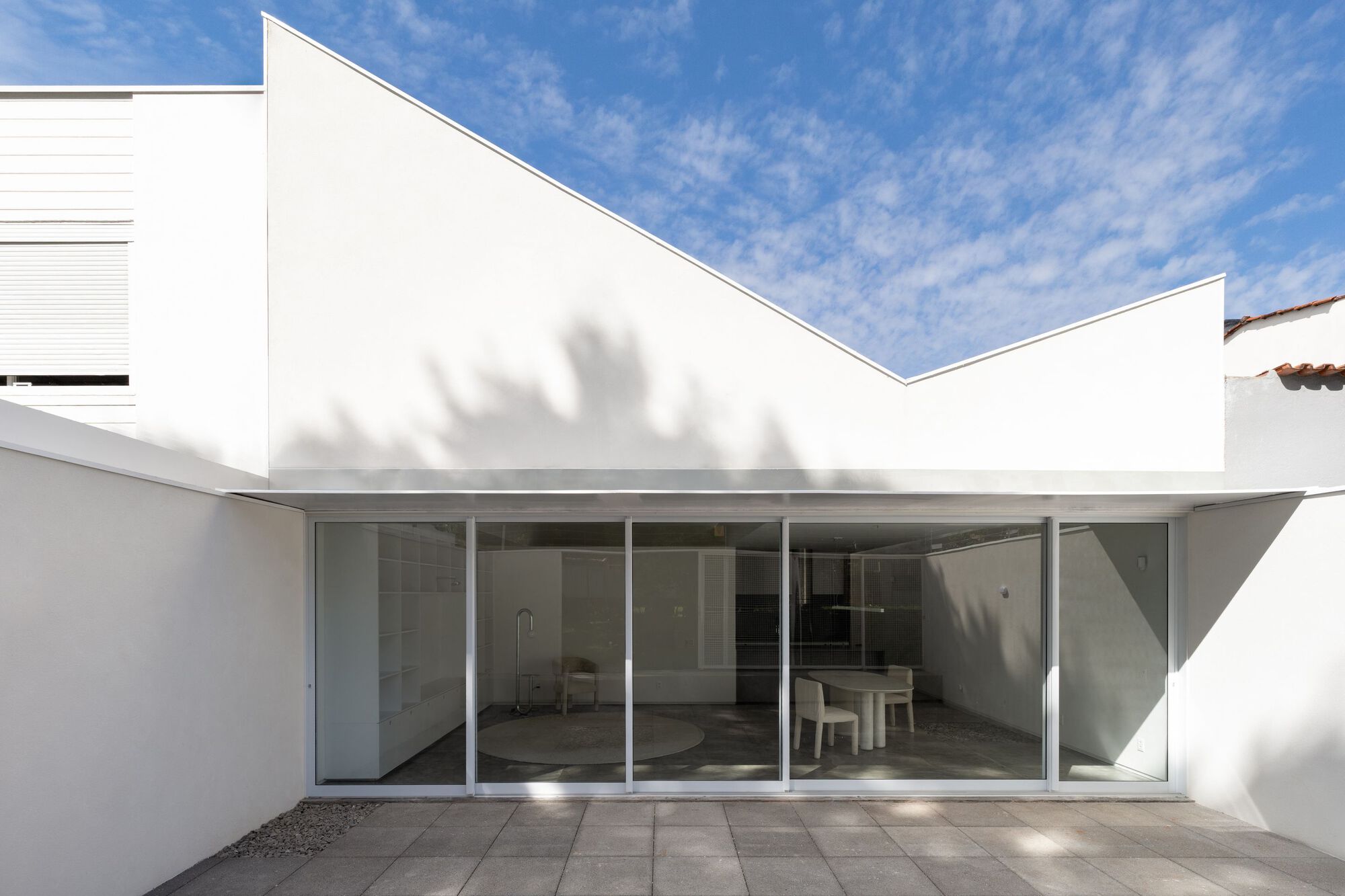 Interior courtyard with full-height glass doors and tree shadow cast across the white parapet walls