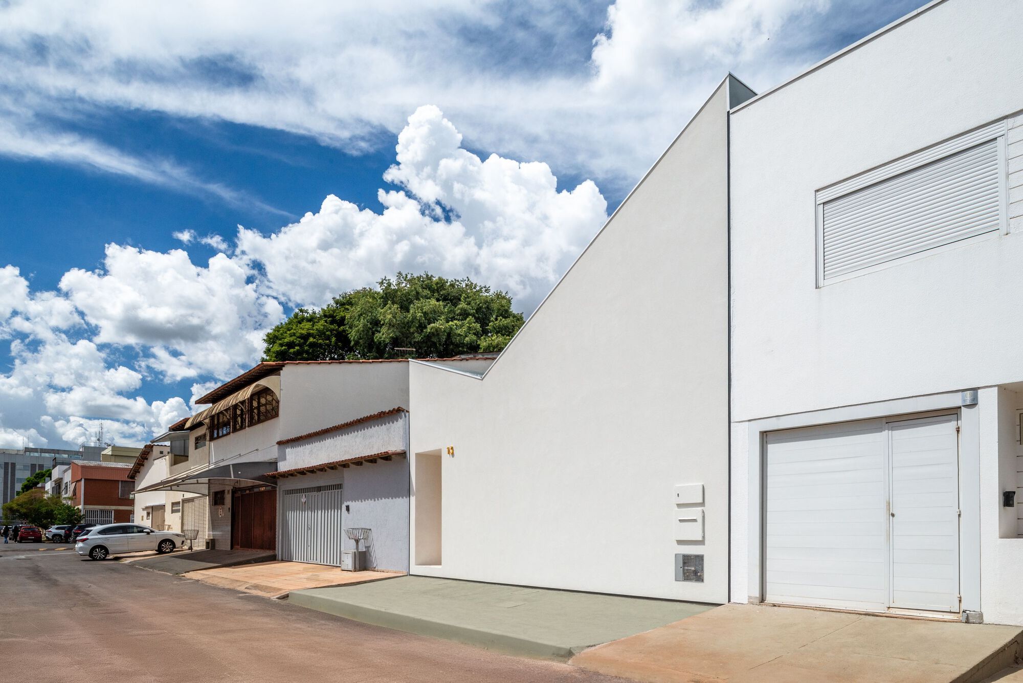 Street view of white volume with triangular roofline beside existing terracotta tiled structures and shopfronts