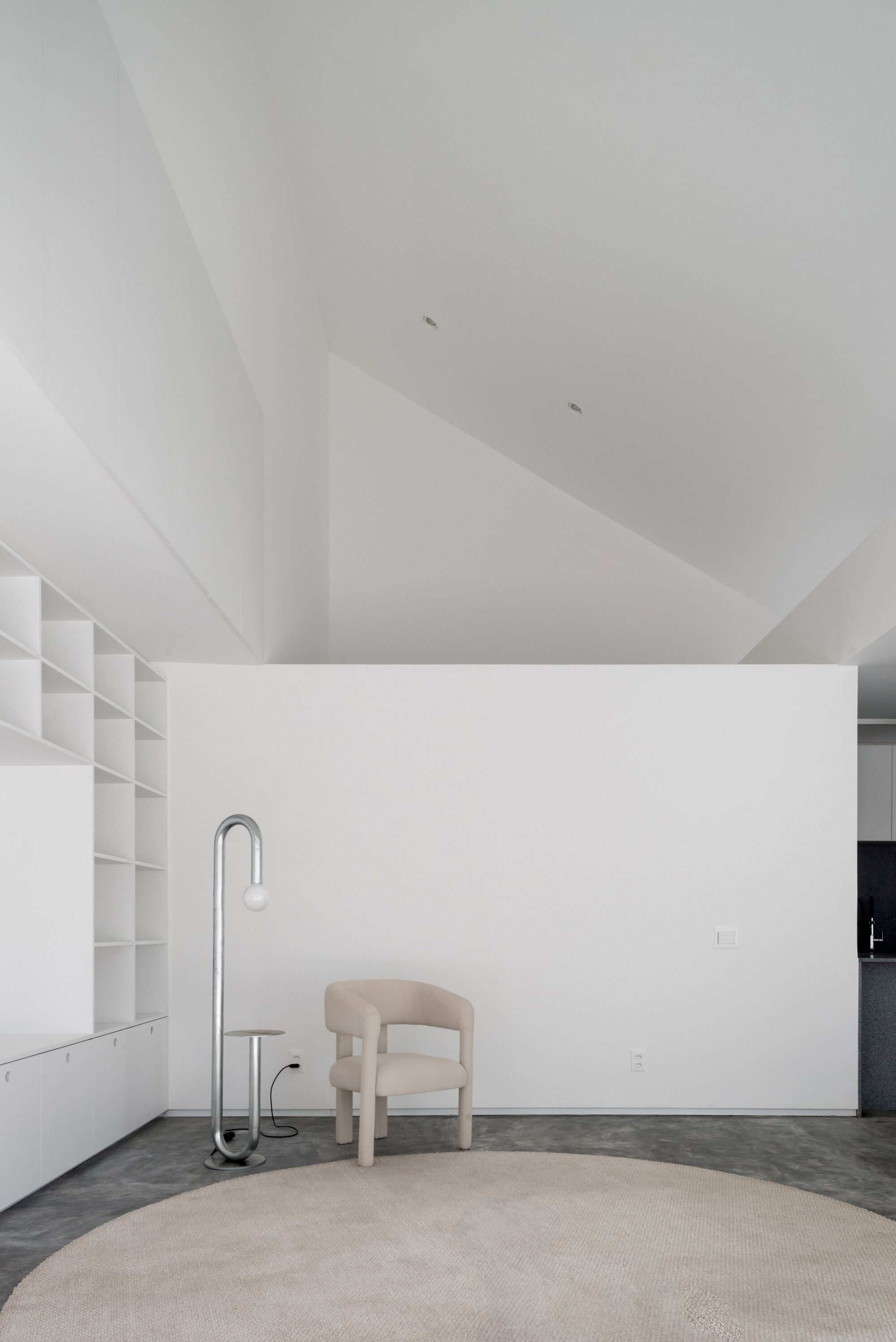 White interior room with faceted ceiling geometry and a beige upholstered chair on a round rug