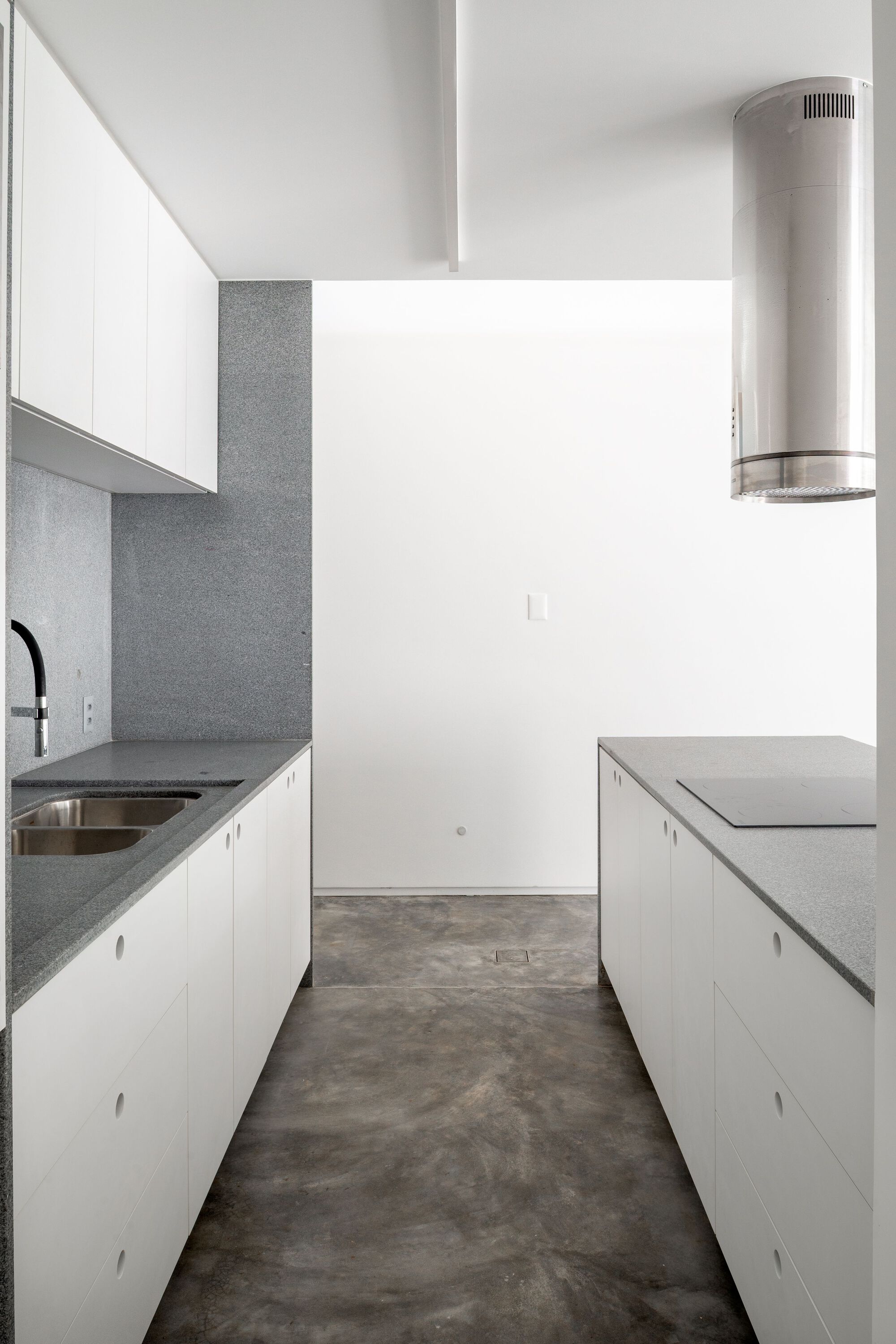 Galley kitchen with white cabinetry, grey terrazzo countertops and a cylindrical stainless steel range hood