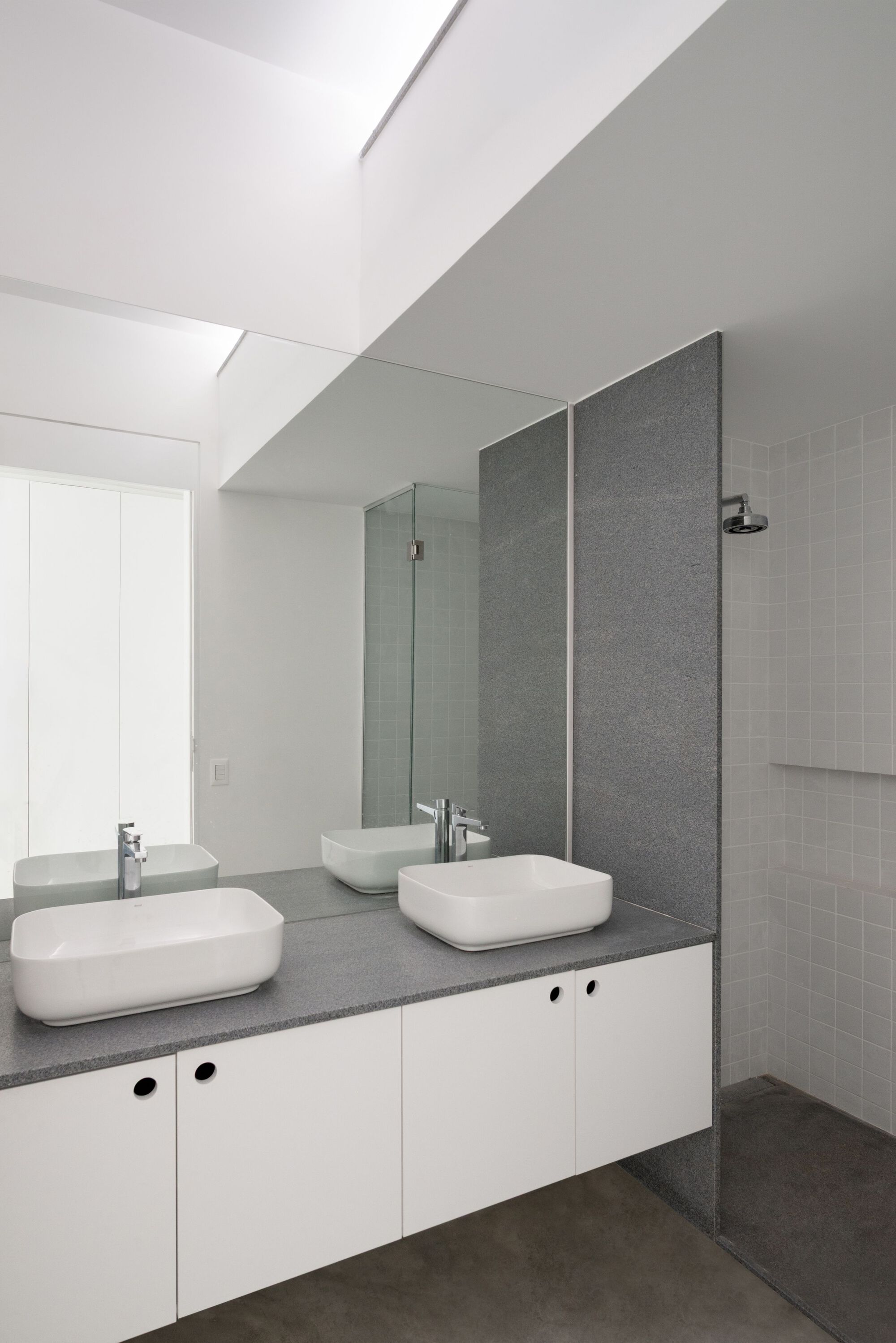 Bathroom vanity with two vessel sinks on grey terrazzo, white tile shower enclosure, and floating mirror