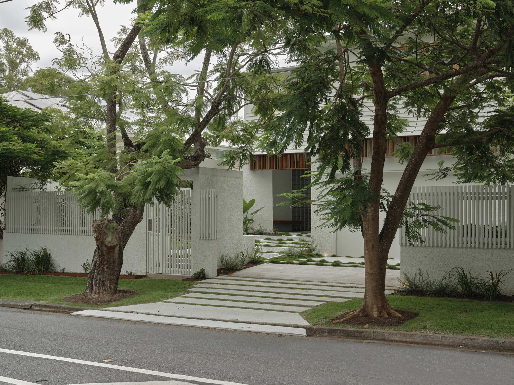 Street entrance framed by mature trees with vertical concrete slat screening and paved pathway