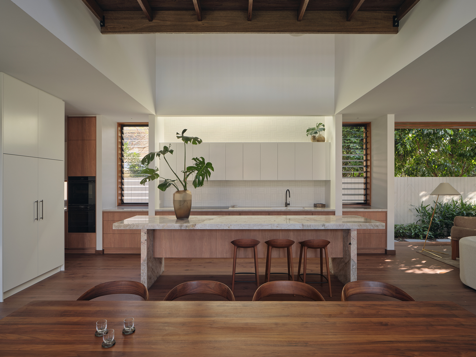Open kitchen and dining area with timber island, exposed roof structure, and planted courtyard beyond
