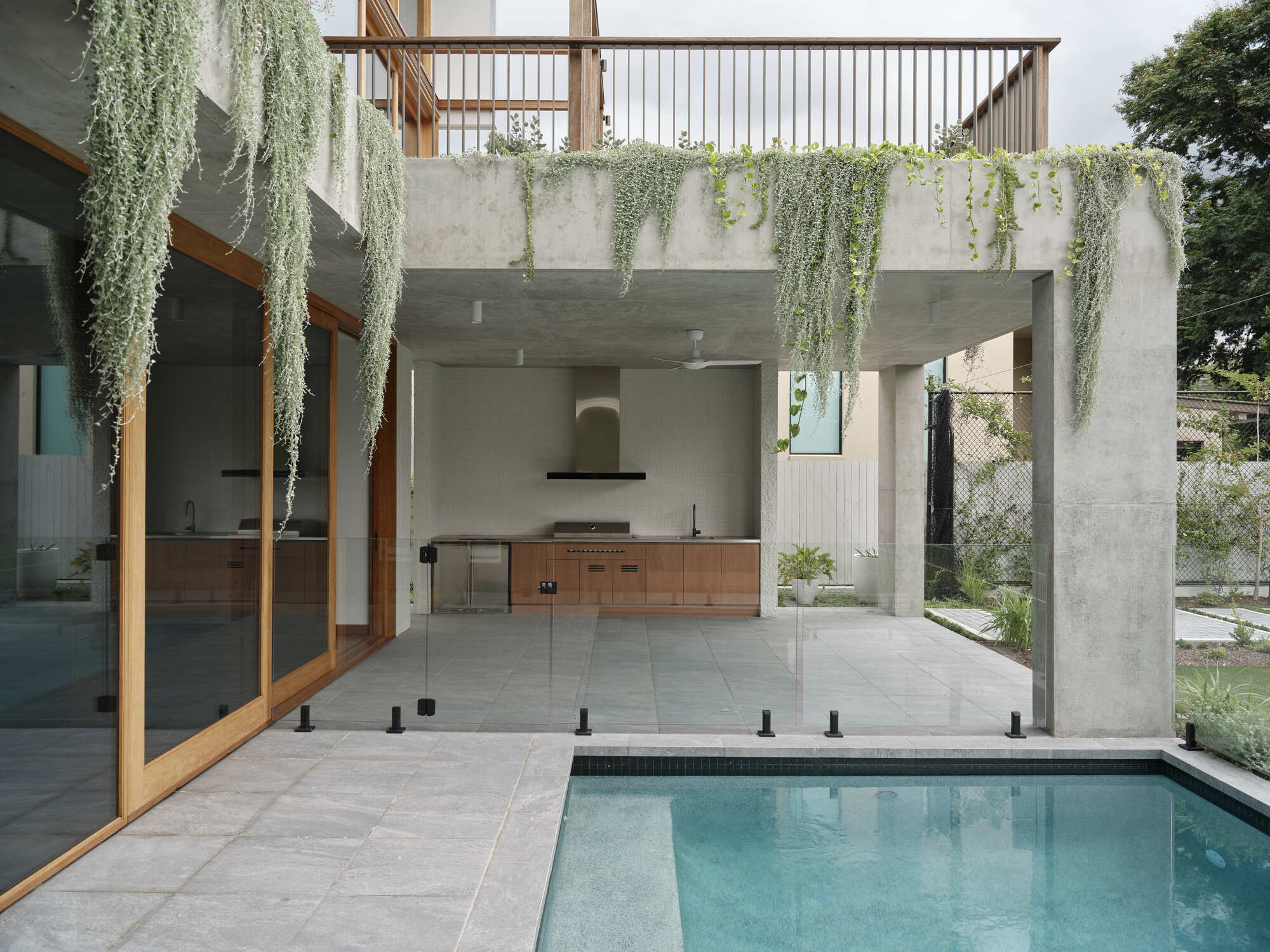 Poolside outdoor kitchen with concrete frame, timber cabinetry, and cascading greenery from upper terrace