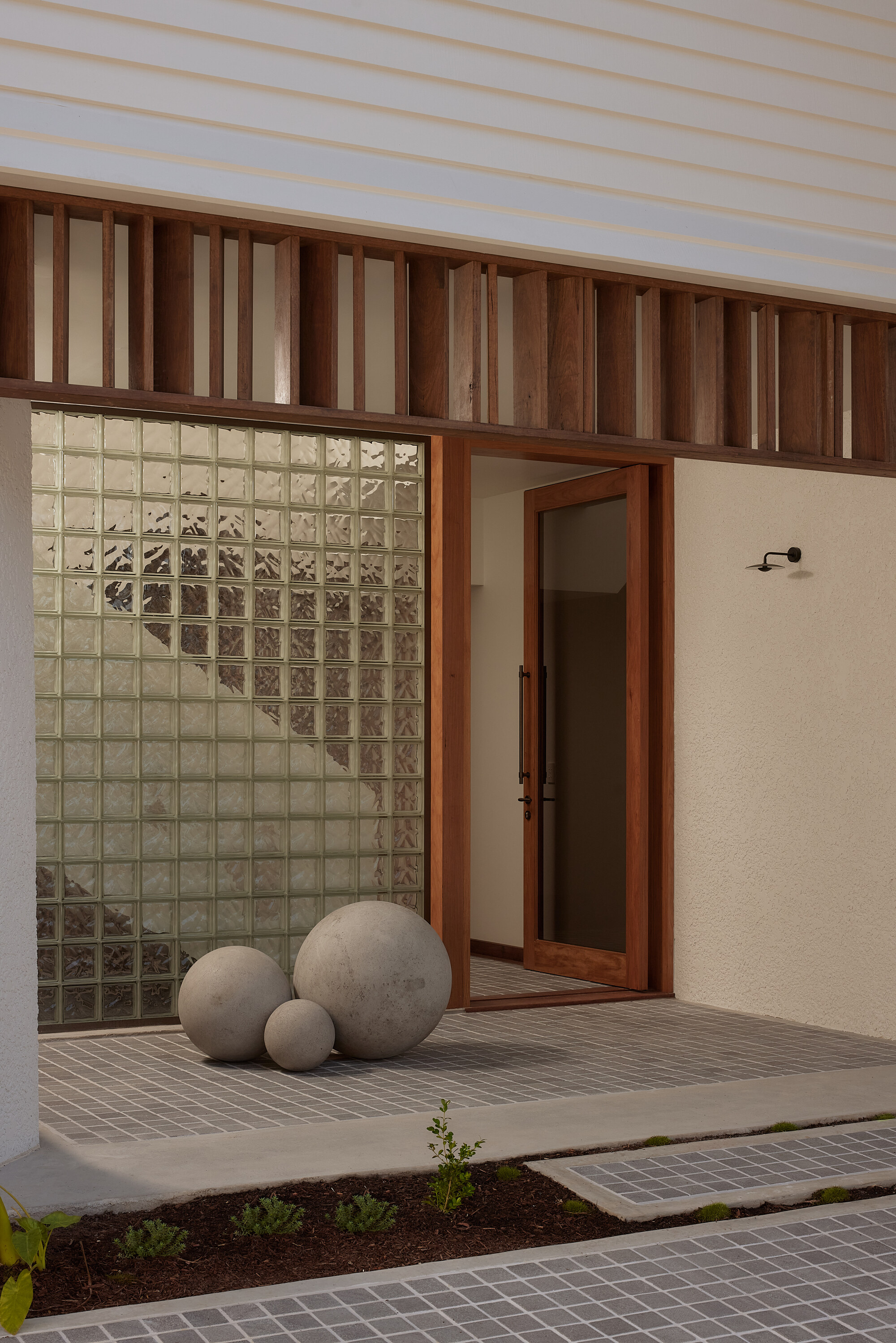 Courtyard entry with glass block window, timber batten screening, and three concrete spheres on timber deck