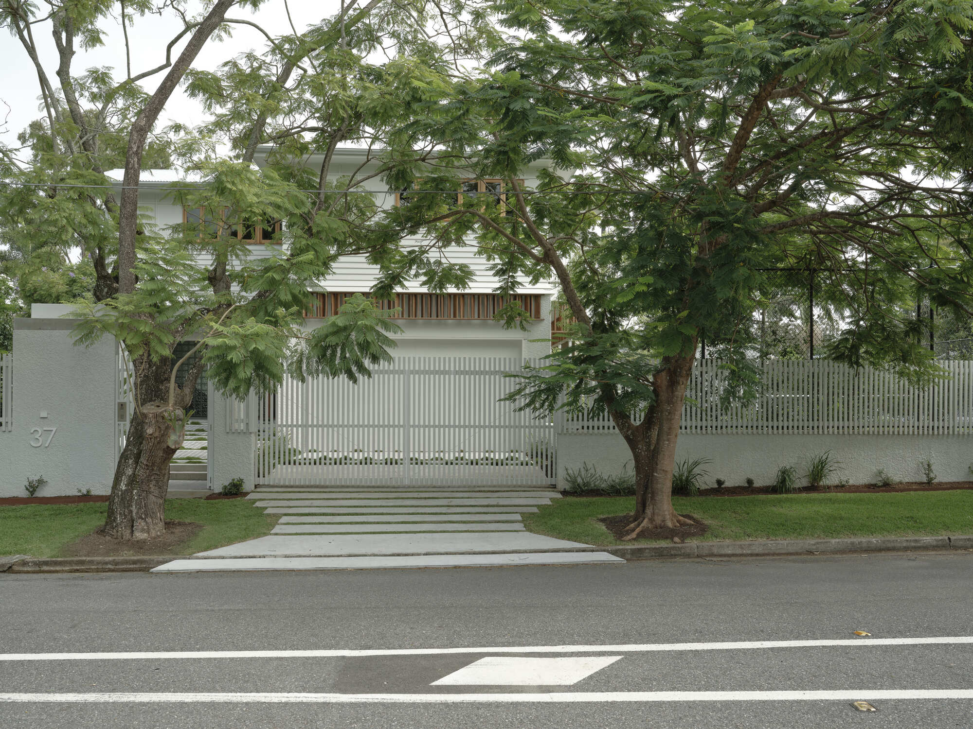 Street view of the white slatted fence and gate flanked by tall trees