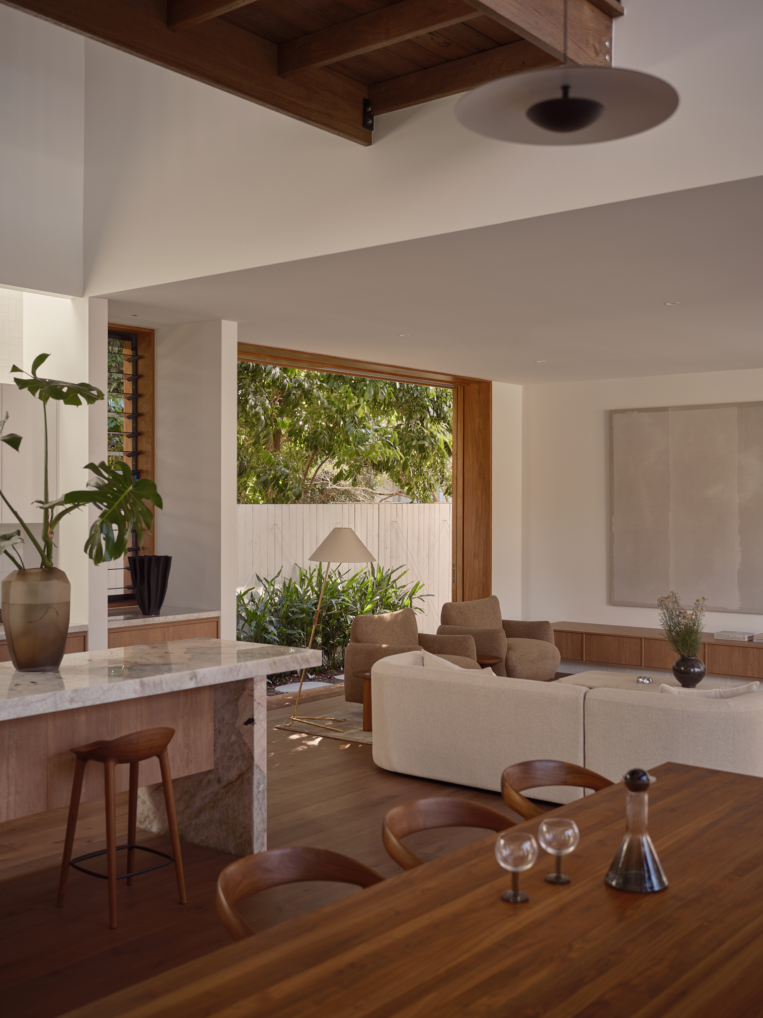 Open plan space showing the dining bar, exposed timber ceiling beam and horizontal window framing greenery
