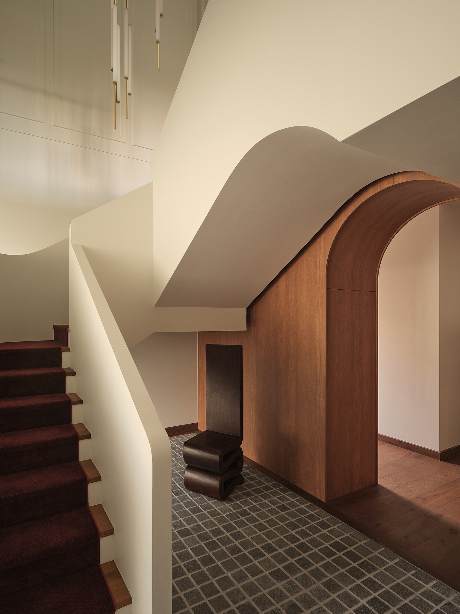 Entry hall with curved timber archway, white plaster staircase and grey mosaic floor tiles