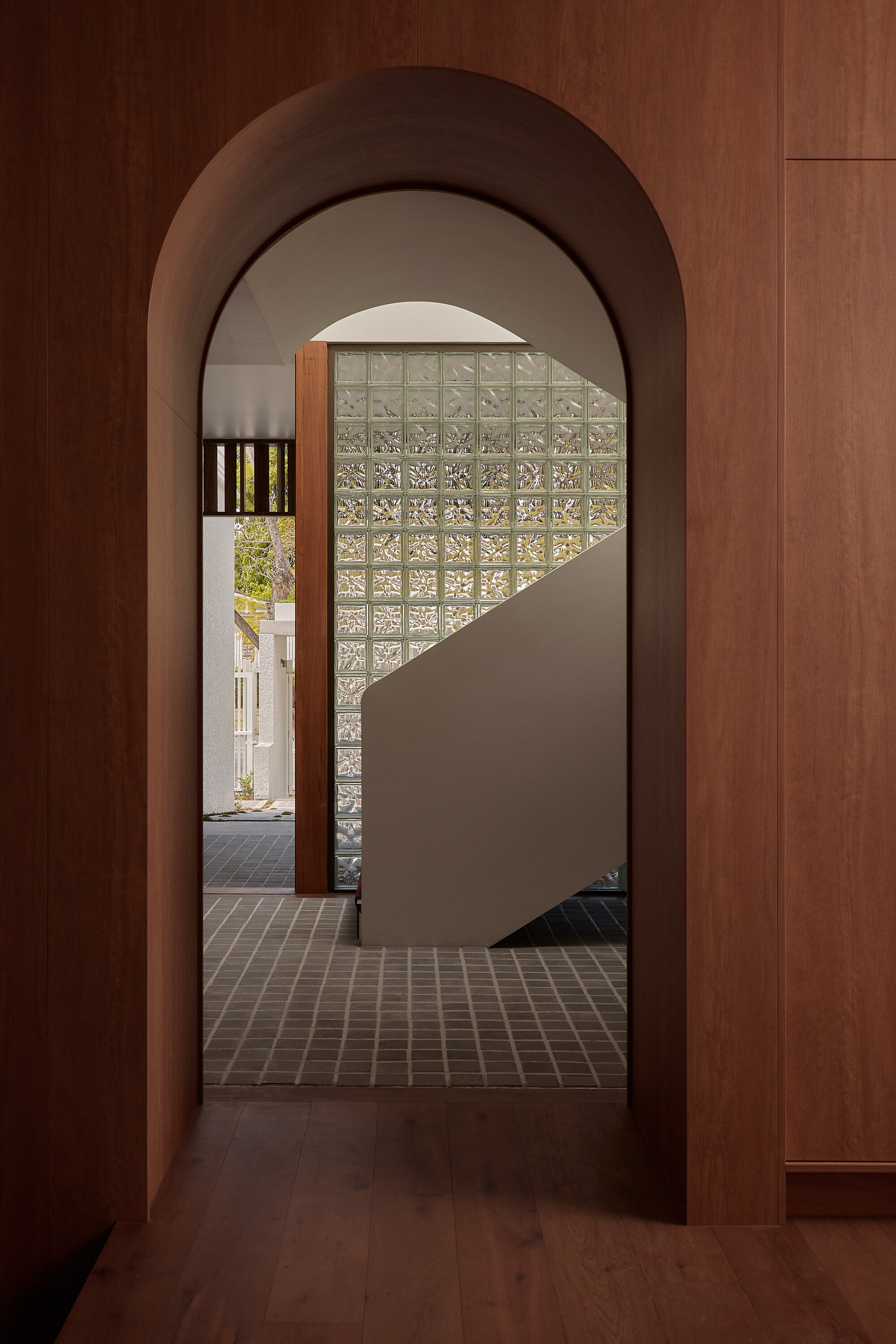 View through arched timber doorway to a curved staircase wall clad in translucent glass blocks