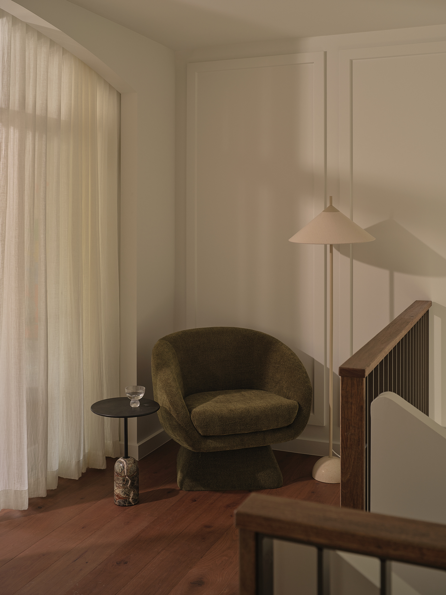Reading corner with upholstered armchair, pendant light, and floor-to-ceiling curtains filtering afternoon light