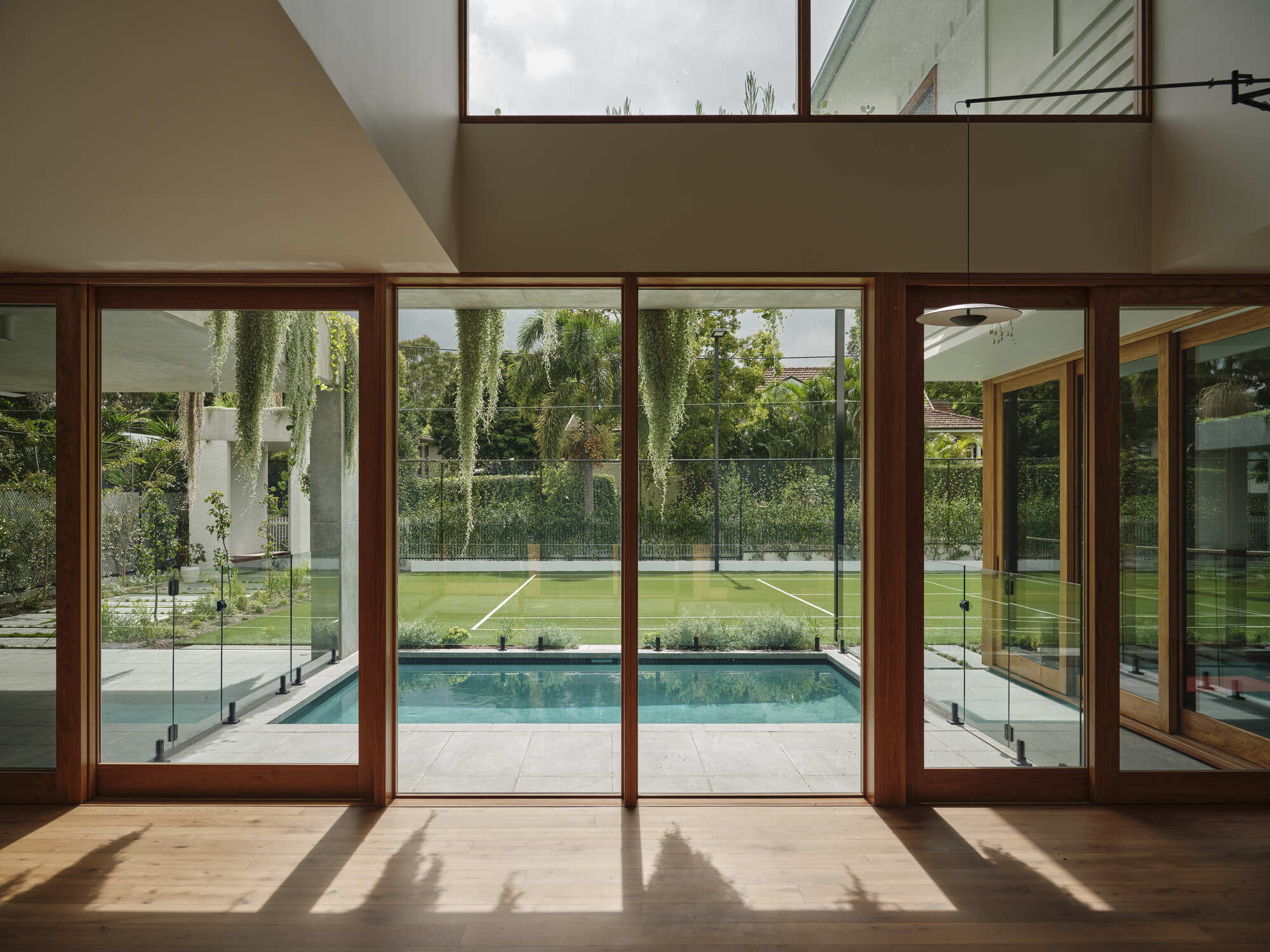 Timber-framed glazed doors overlooking pool and lawn with clerestory windows above casting afternoon shadows