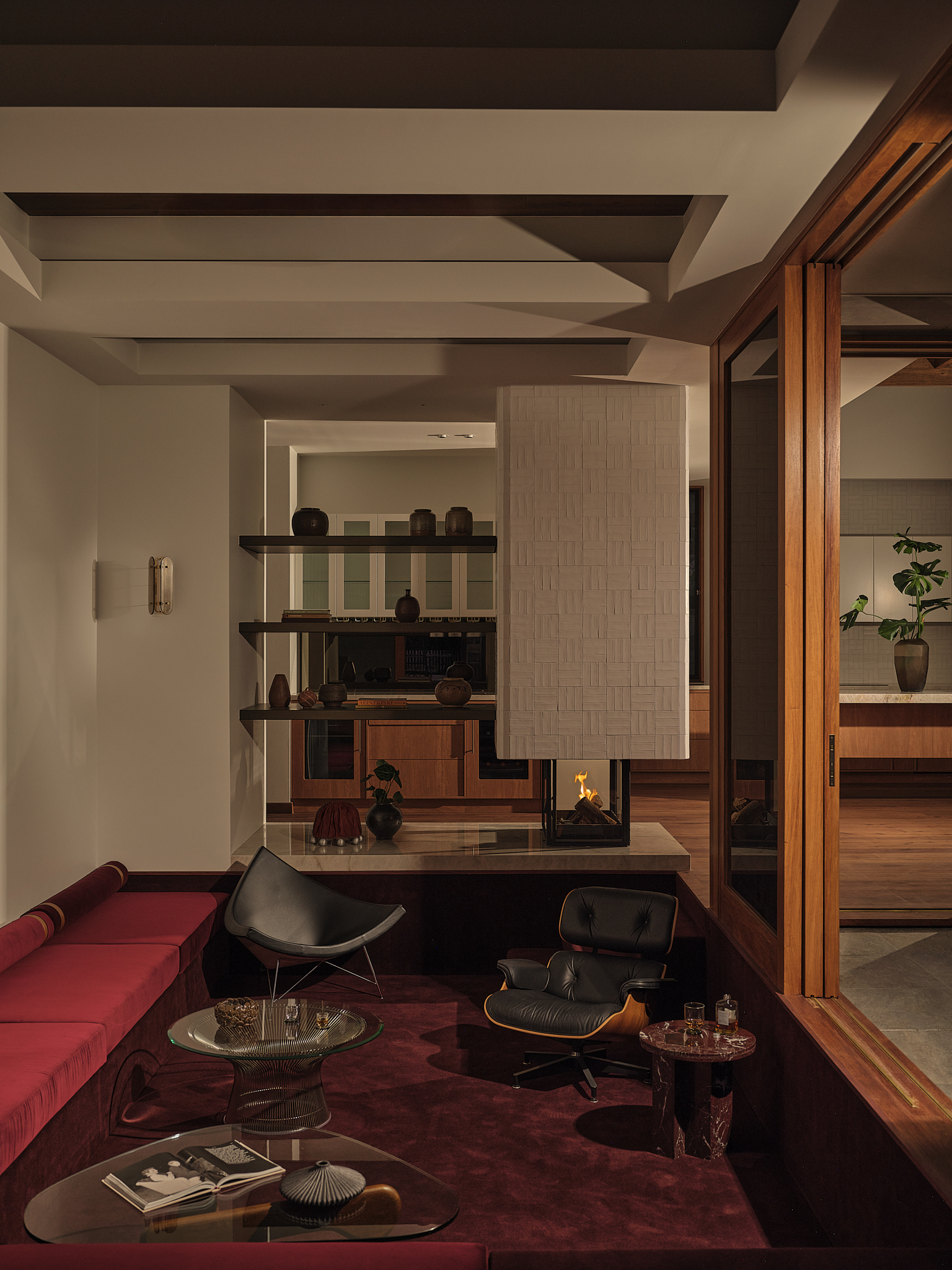 Sunken living area with coffered ceiling, timber-framed glazing and warm evening light on built-in shelving