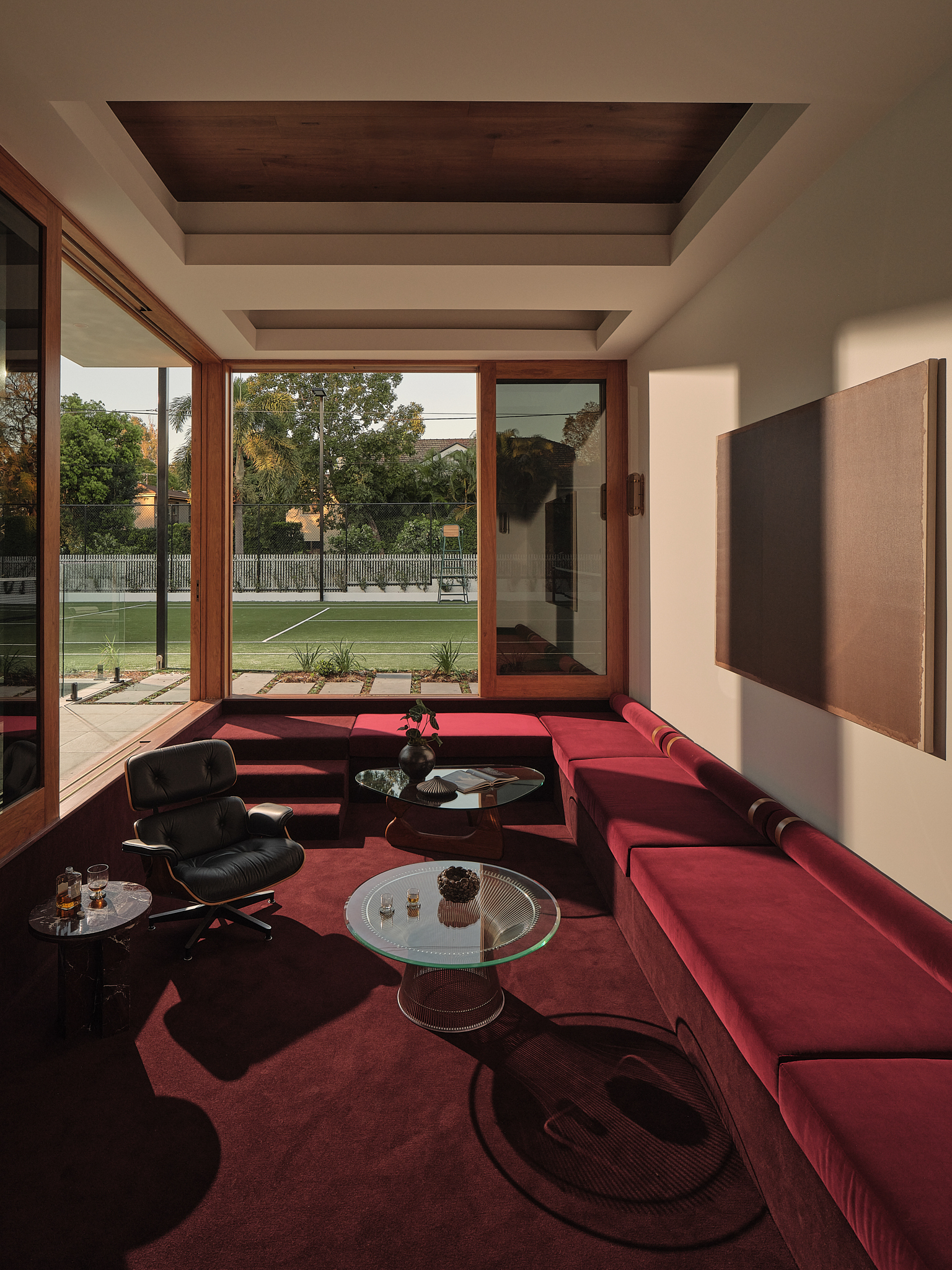 Living space with red upholstered seating, coffered ceiling and timber sliding doors opening to lawn at dusk