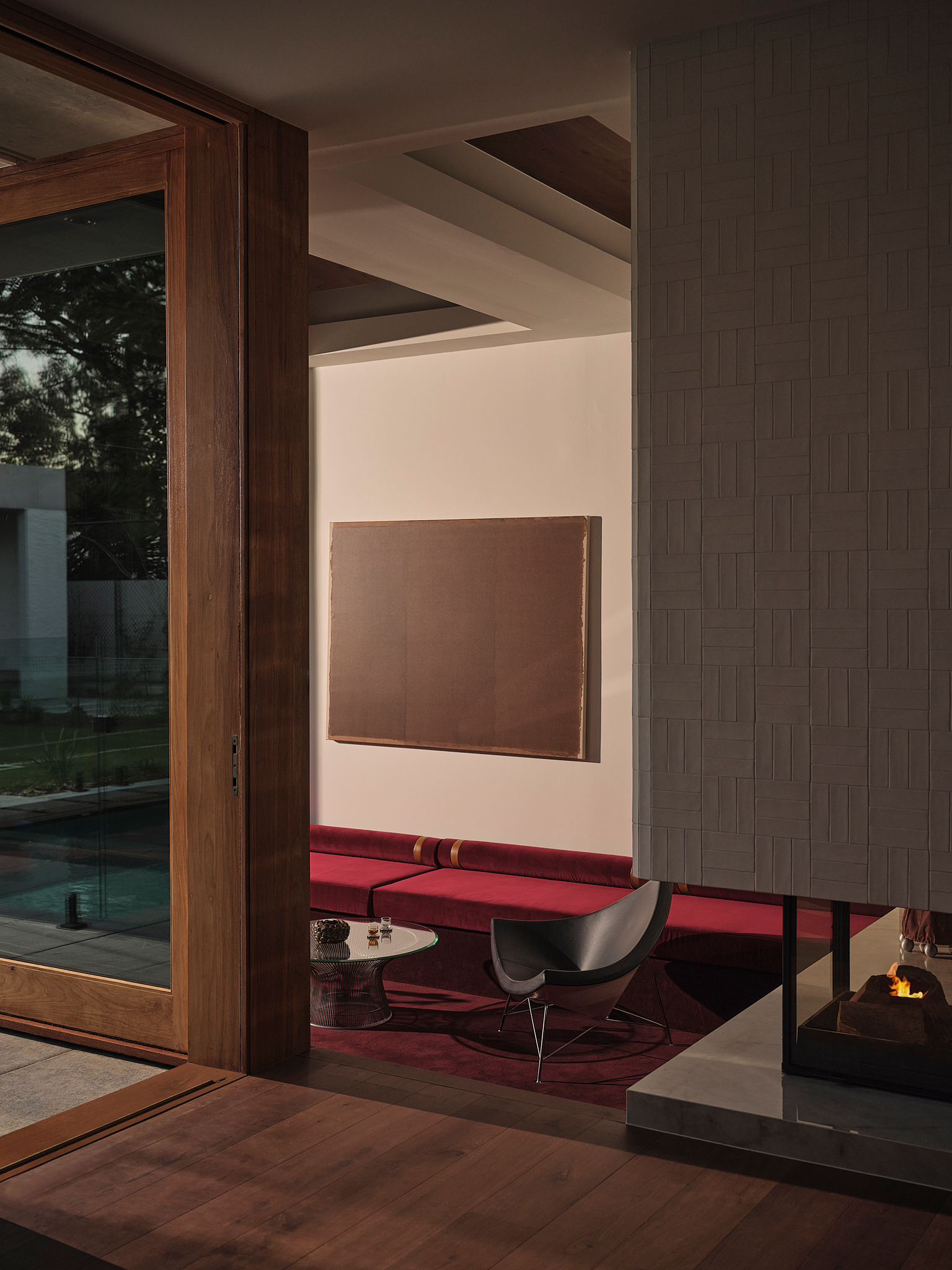 Interior corner showing timber door frame, woven tile wall panel and view through to seating in evening light
