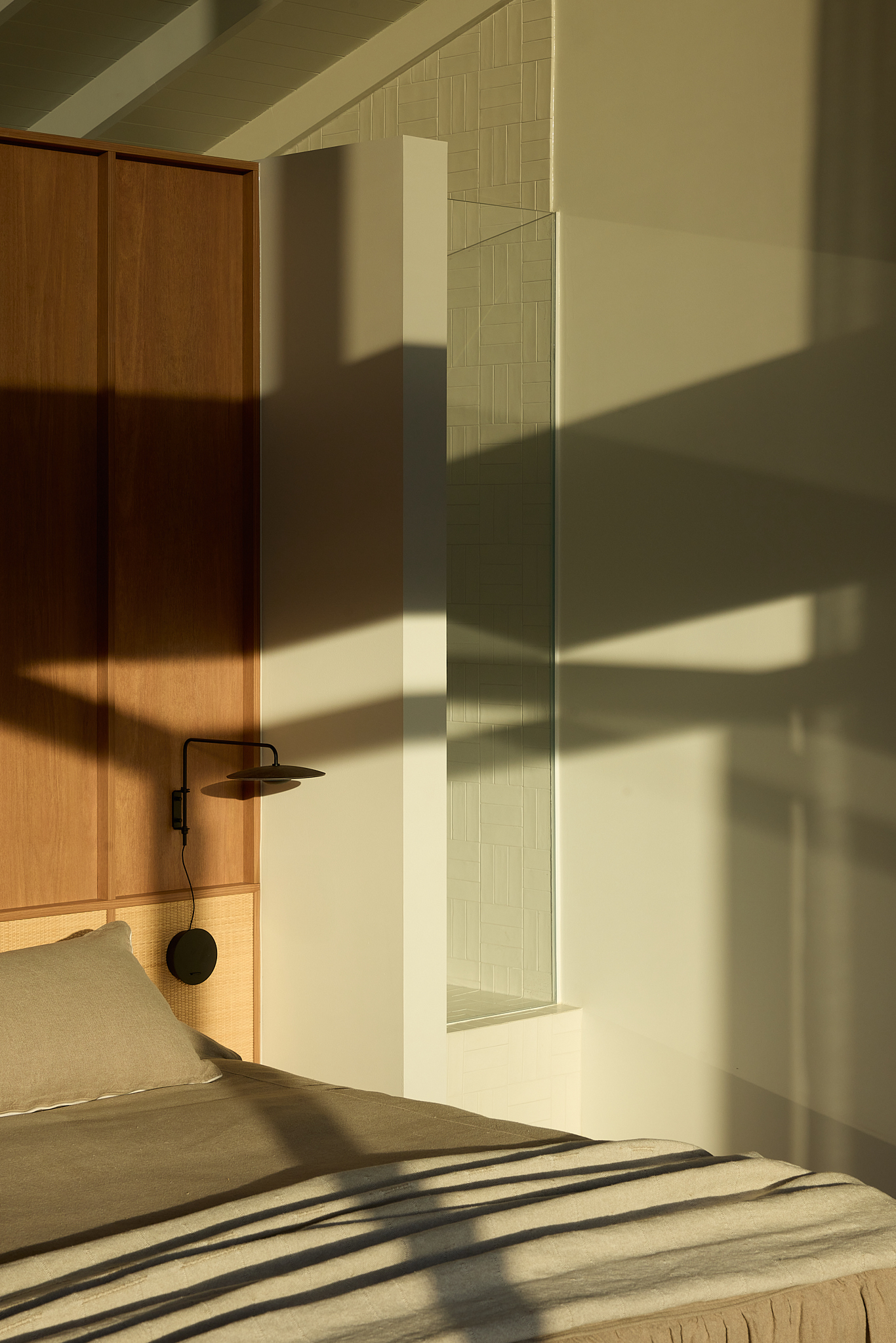Bedroom with timber cabinetry and warm afternoon sunlight casting strong shadows across bed and walls