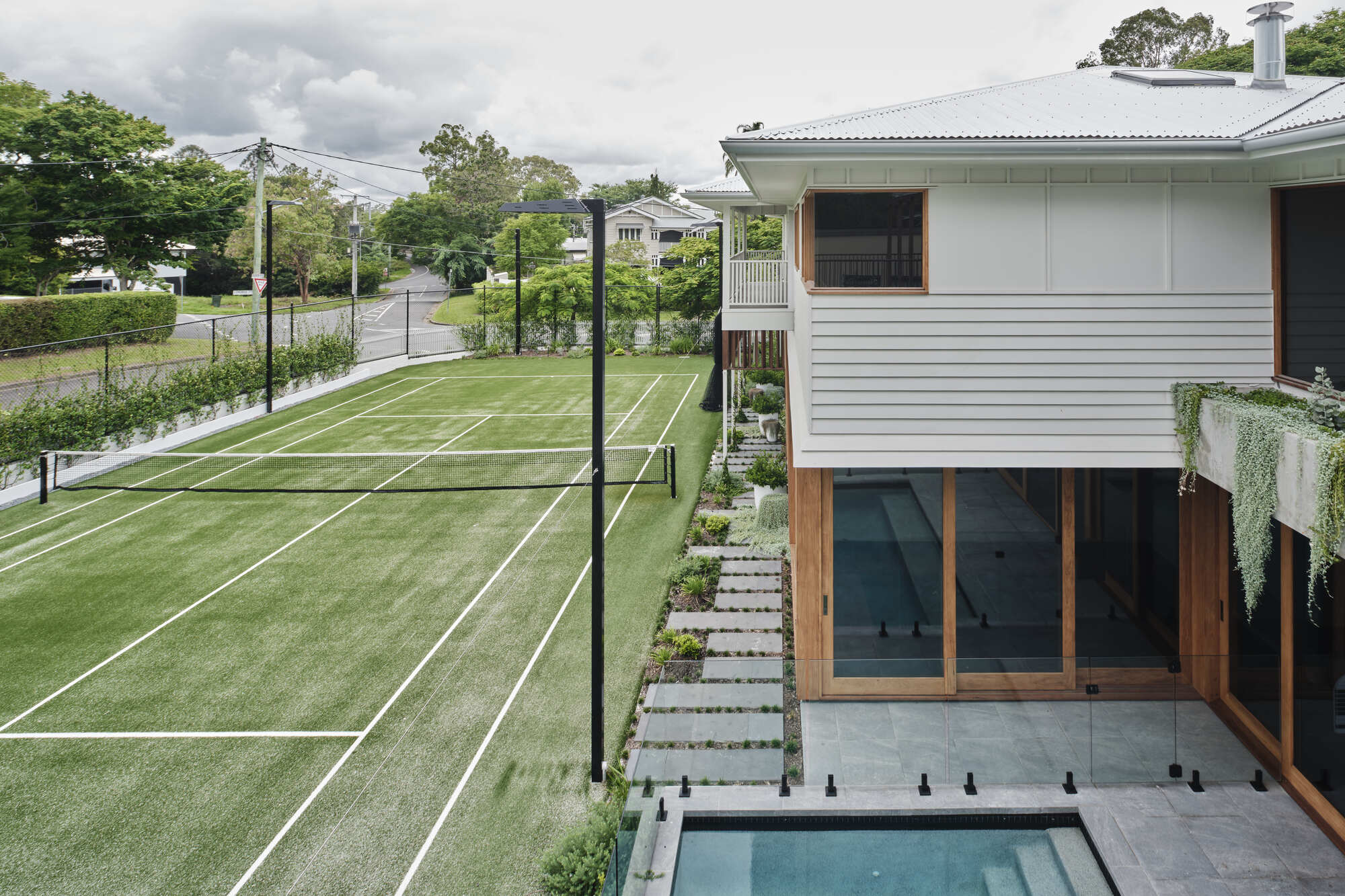 Elevated rear terrace with plunge pool and timber-framed glazing overlooking a grass tennis court
