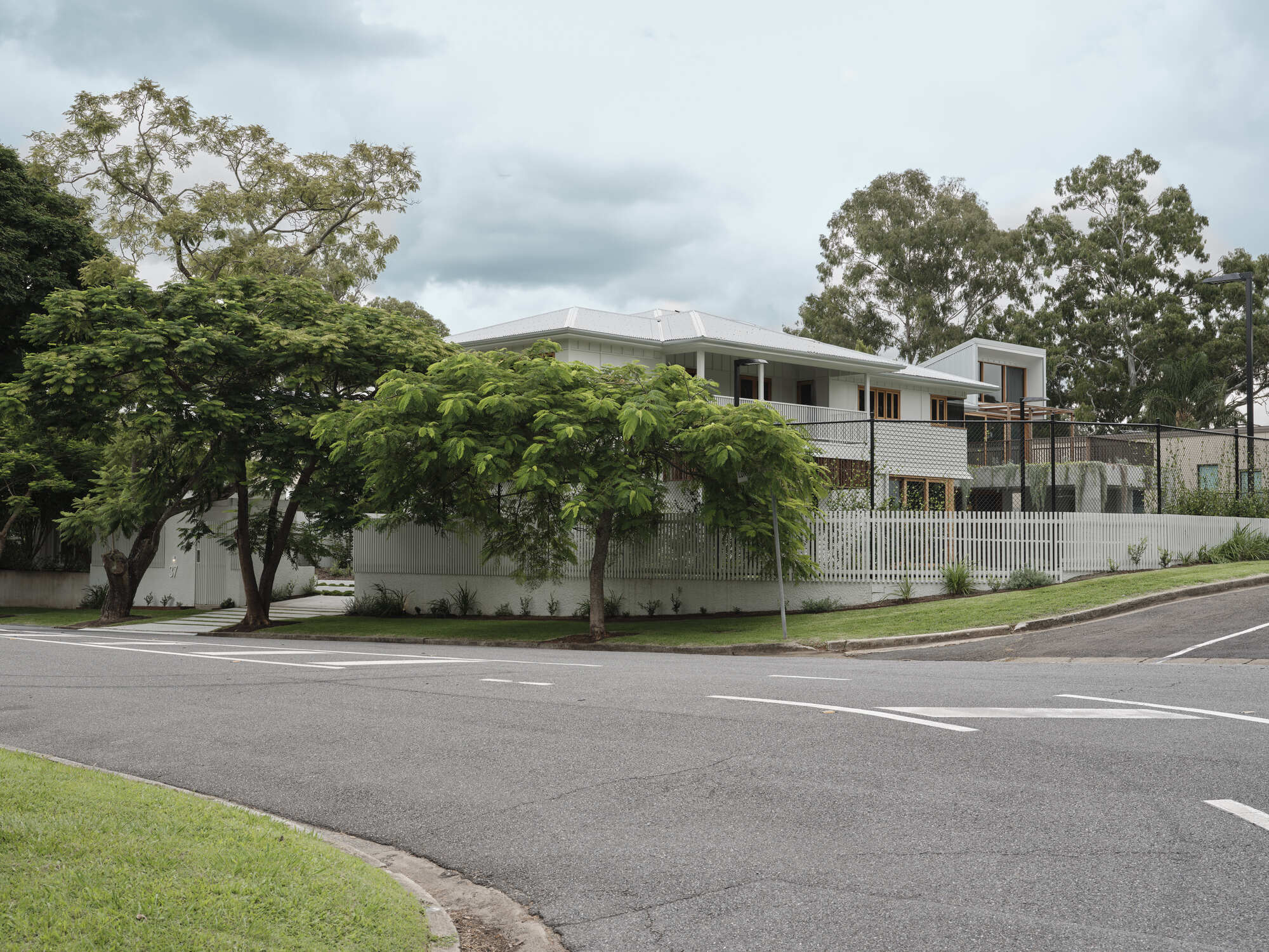 Street corner view showing white weatherboard cladding and corrugated metal roof beneath mature trees