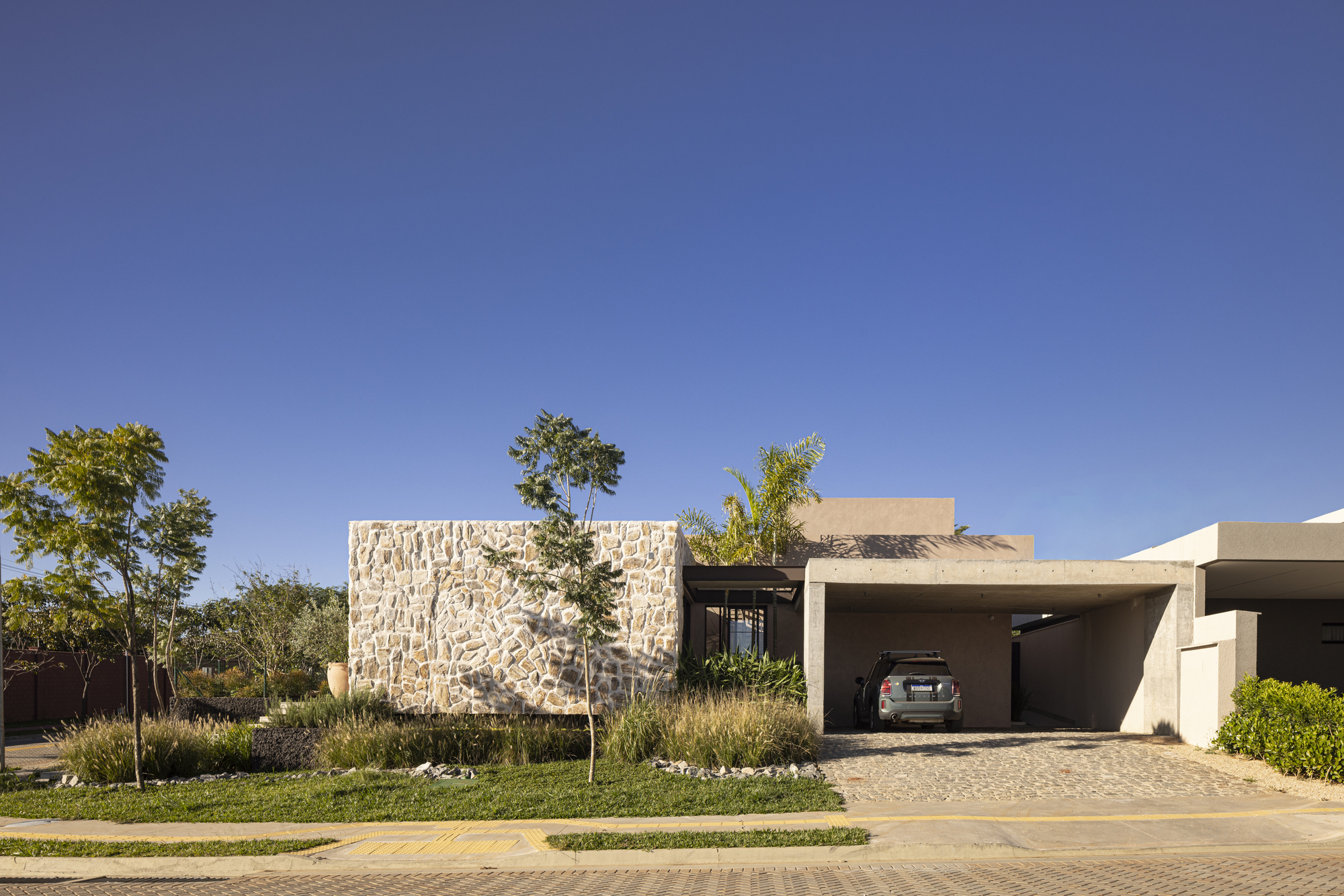 Street view of the textured stone wall and covered carport under a clear blue sky