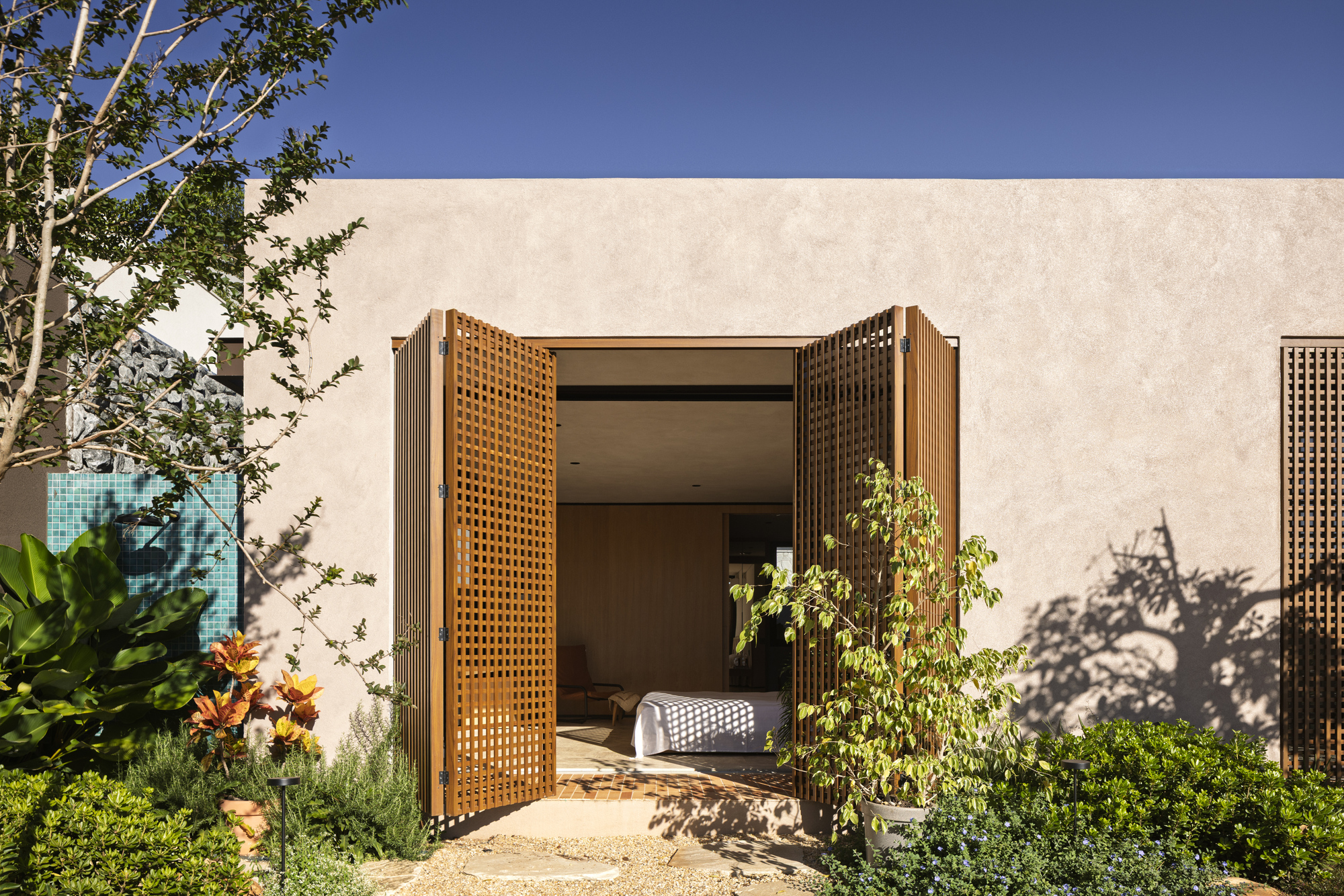 Perforated timber screens framing a bedroom entrance with tree shadows on the stucco wall