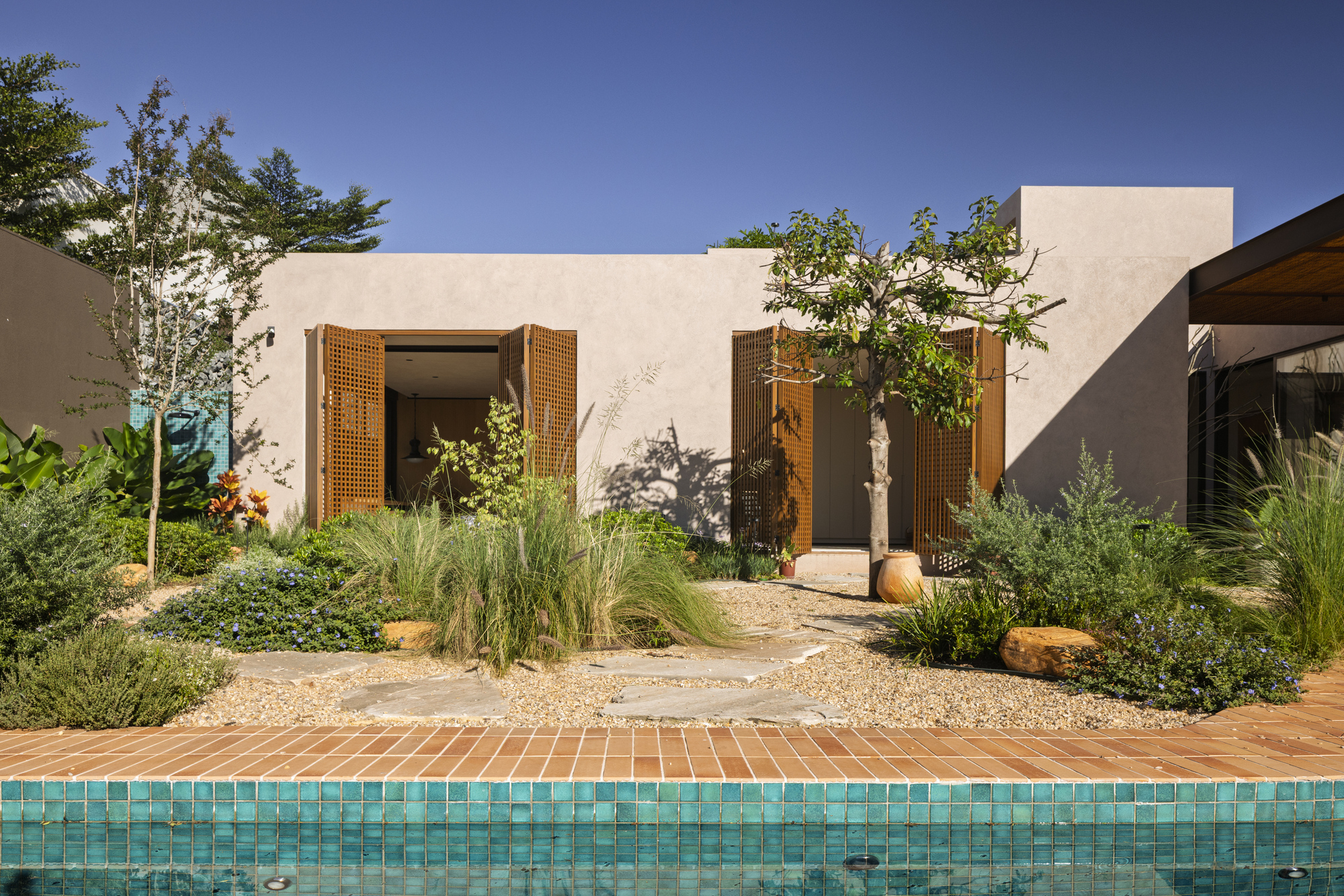 Poolside view of the courtyard facade with lattice shutters and native grasses in a gravel garden bed